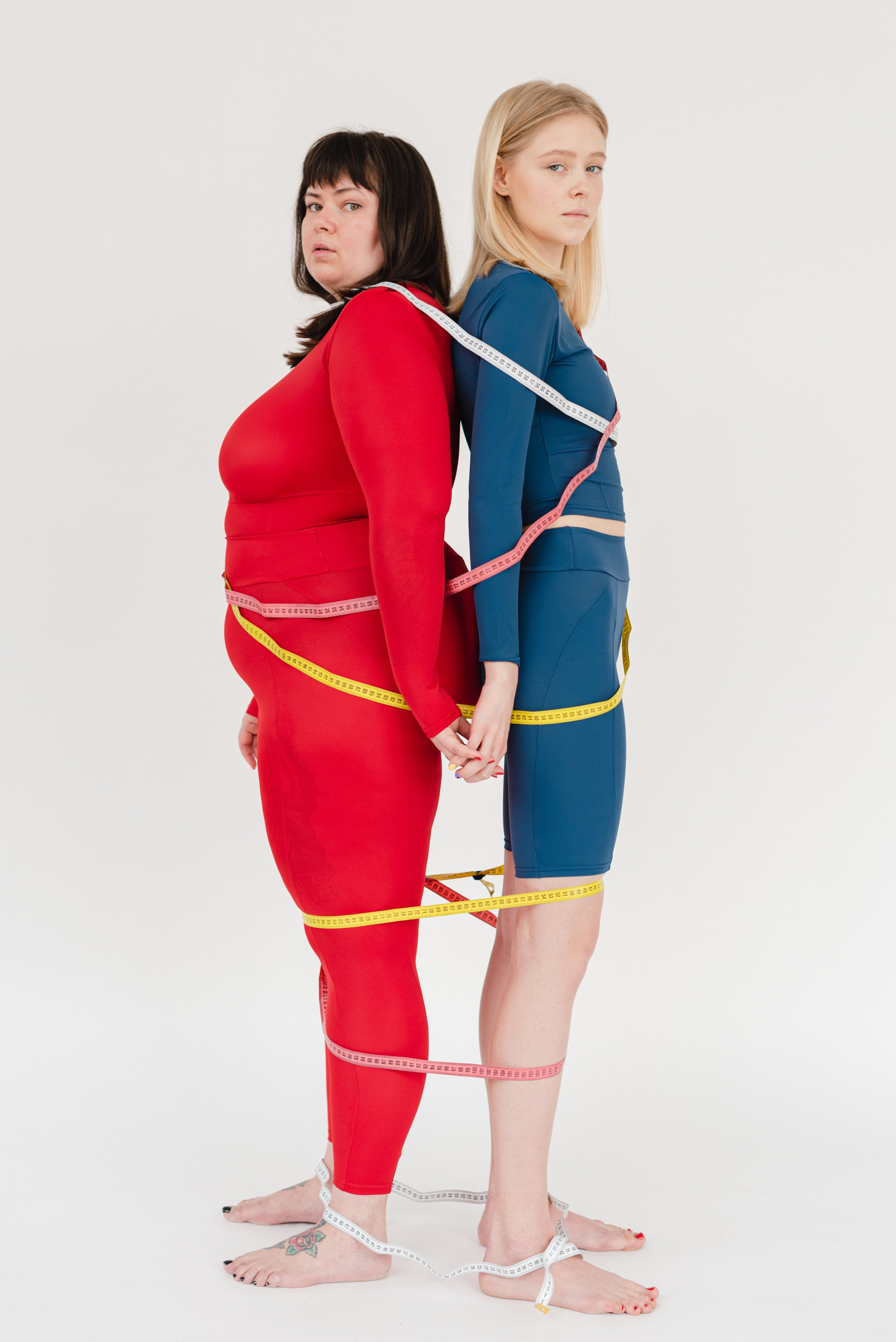Two women standing back to back with measuring tapes around them. | Source: Pexels