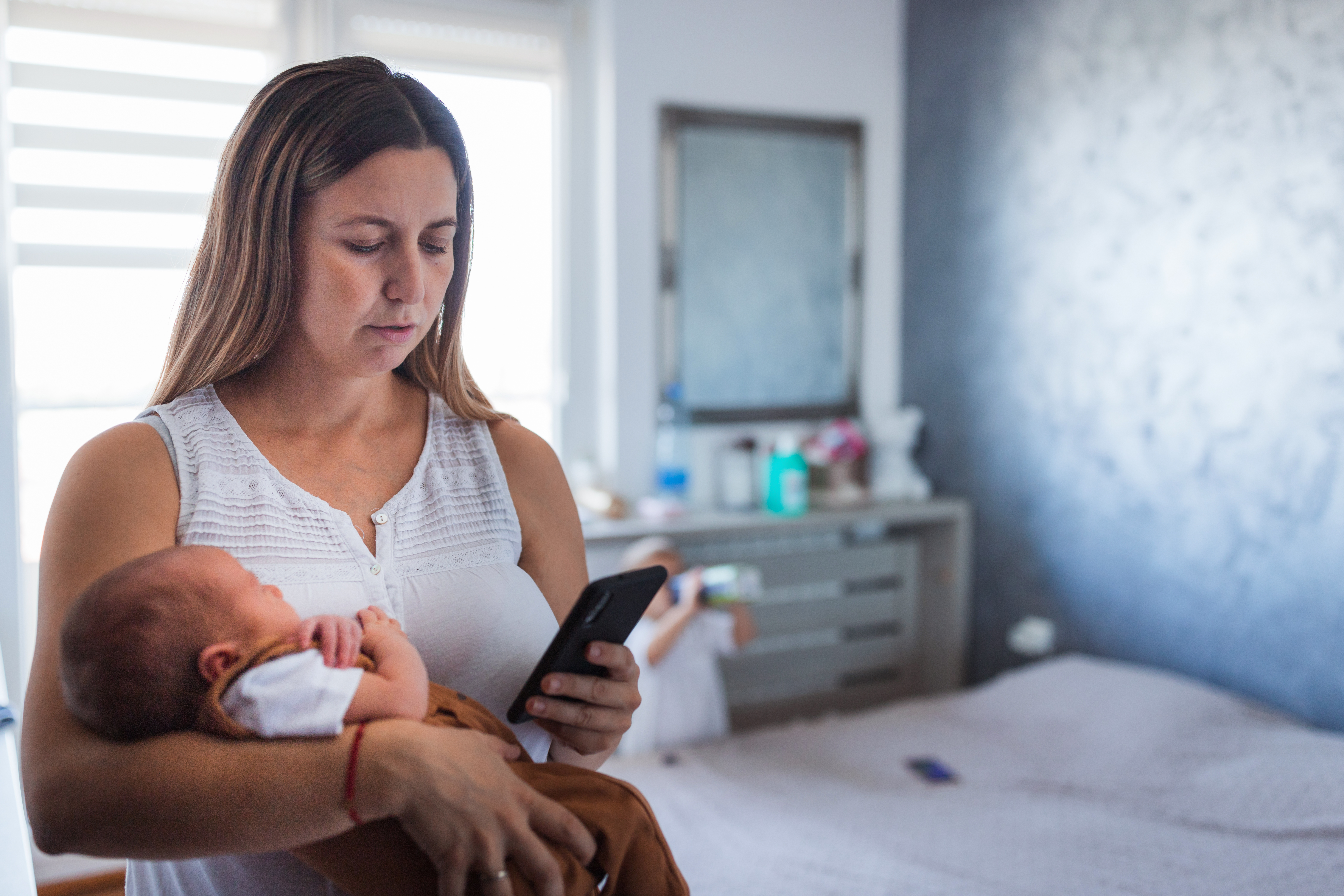 A woman holding a baby while looking at her phone | Source: Getty Images