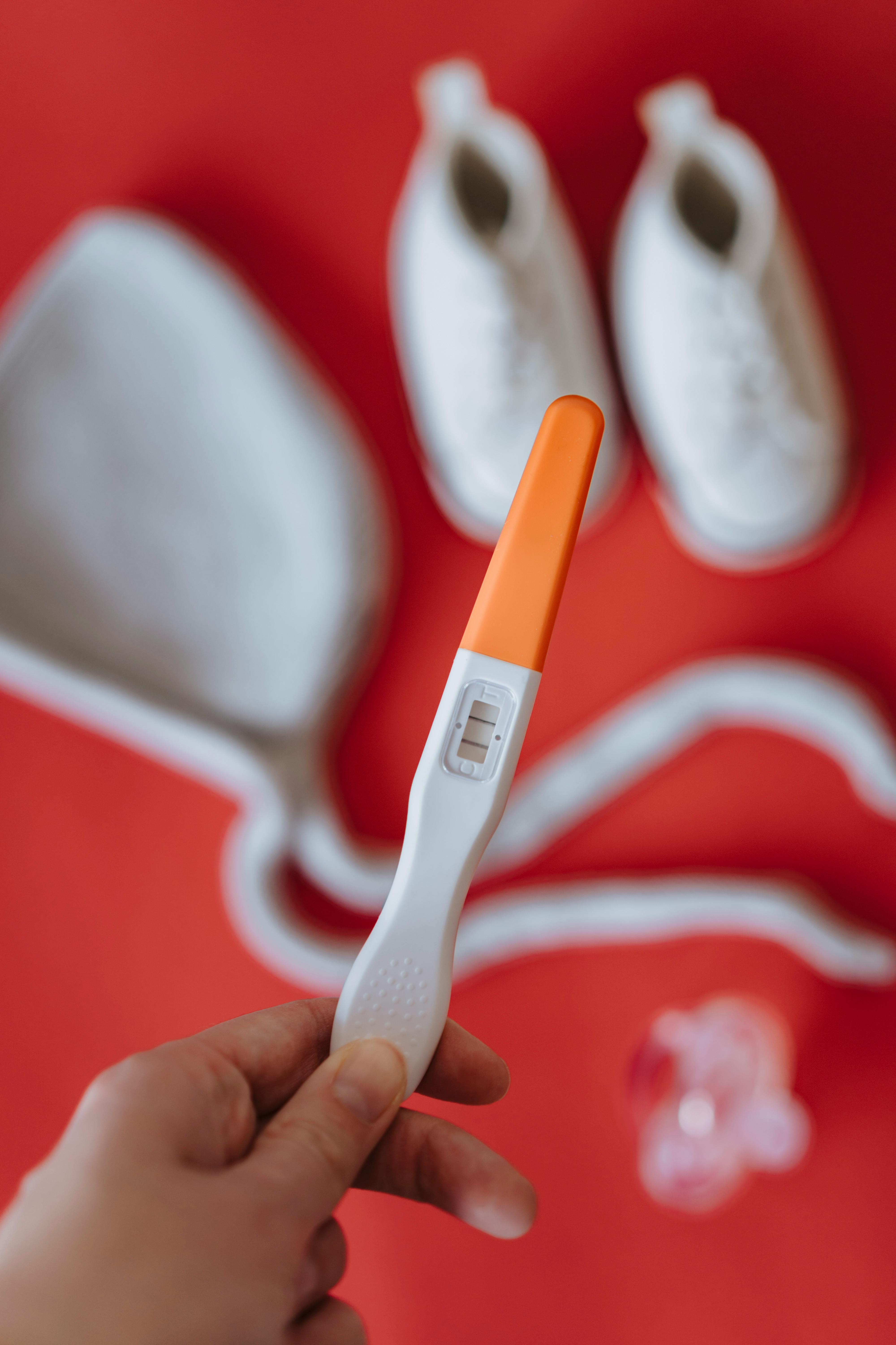 Someone holding positive pregnancy test while baby clothes appear faded in the background | Source: Pexels