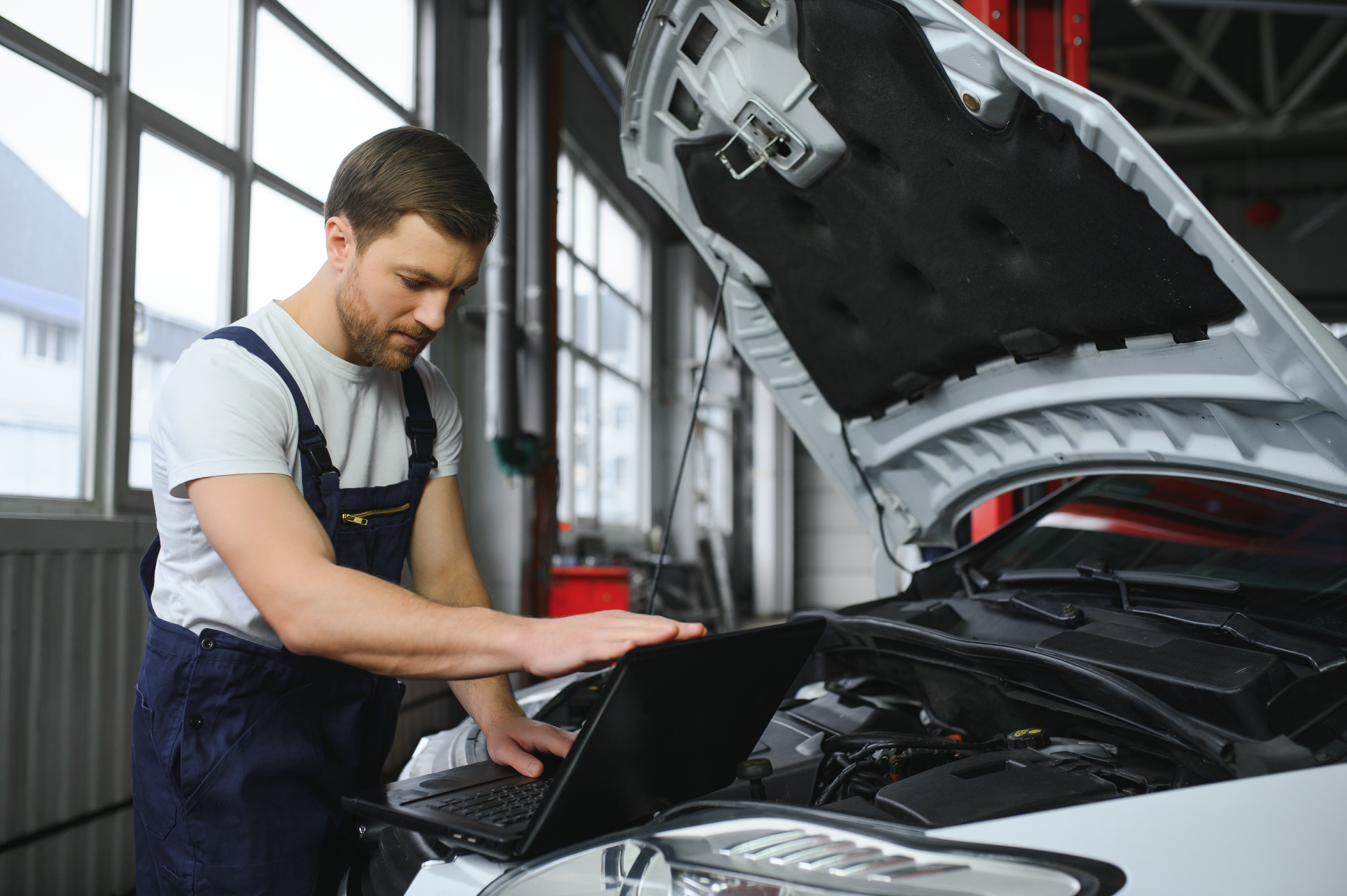 Mechanic man mechanic manager worker using a laptop computer checking car in workshop at auto car repair service center. Engineer young man looking at inspection vehicle details under car hood | Source: Shutterstock