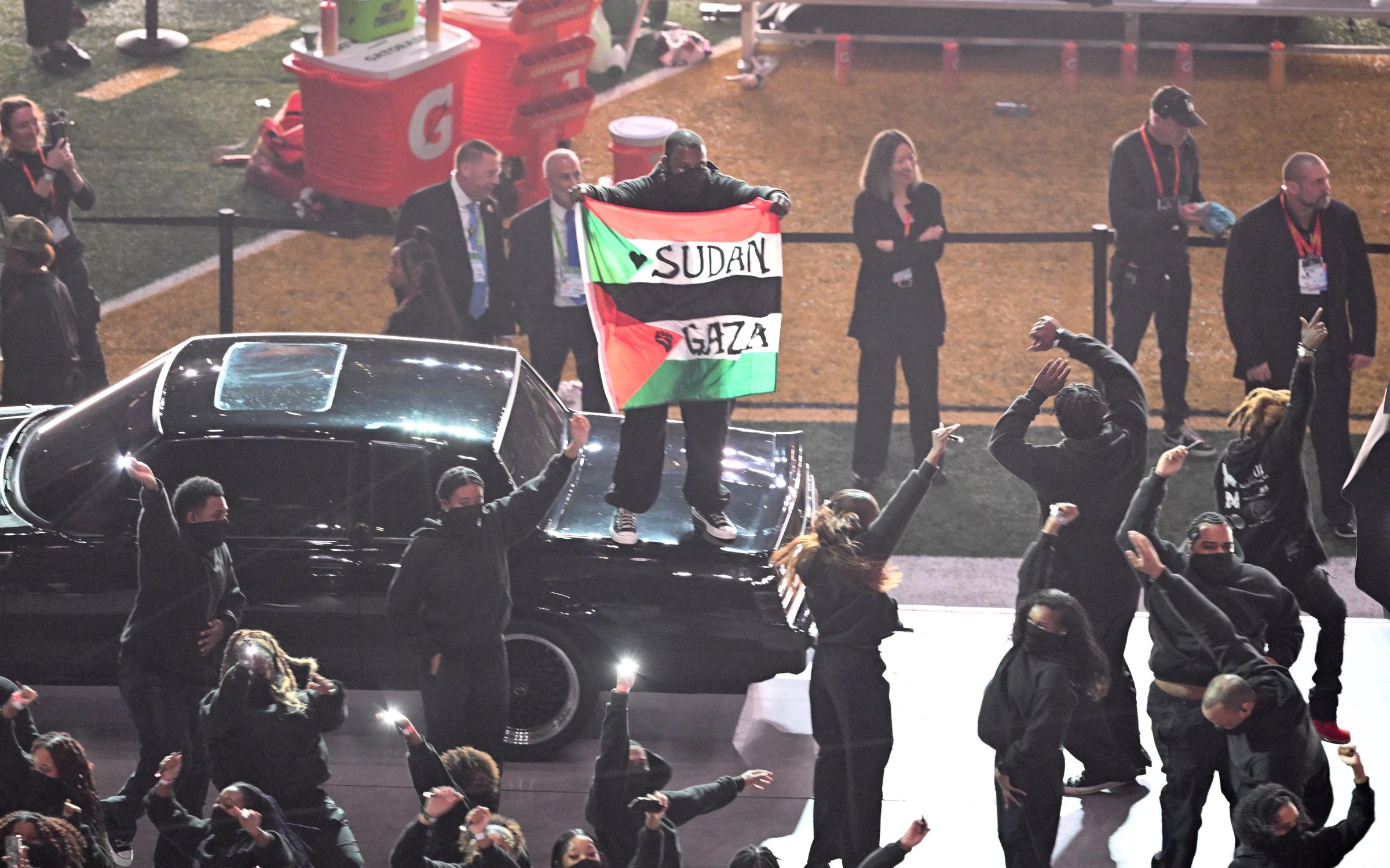 A protestor holds a Palestinian flag with the words "Gaza" and "Sudan" as Kendrick Lamar performs on February 9, 2025 | Source: Getty Images