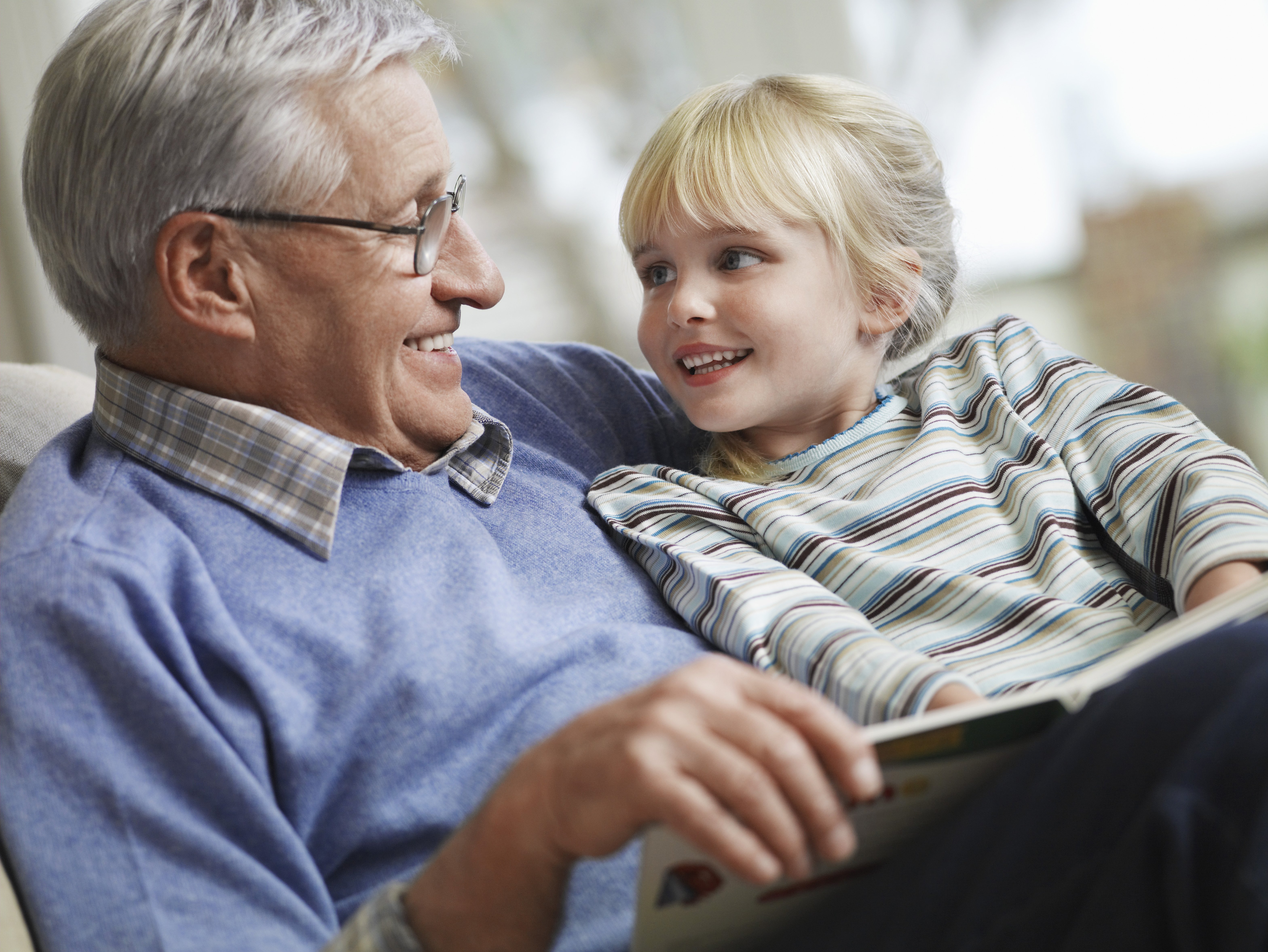Happy little girl with grandfather reading story book at home | Photo: Shutterstock.com