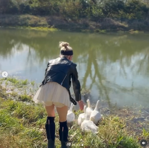 Osbourne tended to a group of white ducks gathered at the edge of the farm's pond, crouching toward the birds as they approached the water. Dressed in boots and a black leather jacket, she appeared fully immersed in caring for the animals that have become part of her family's everyday country life. | Source: Instagram/kellyosbourne