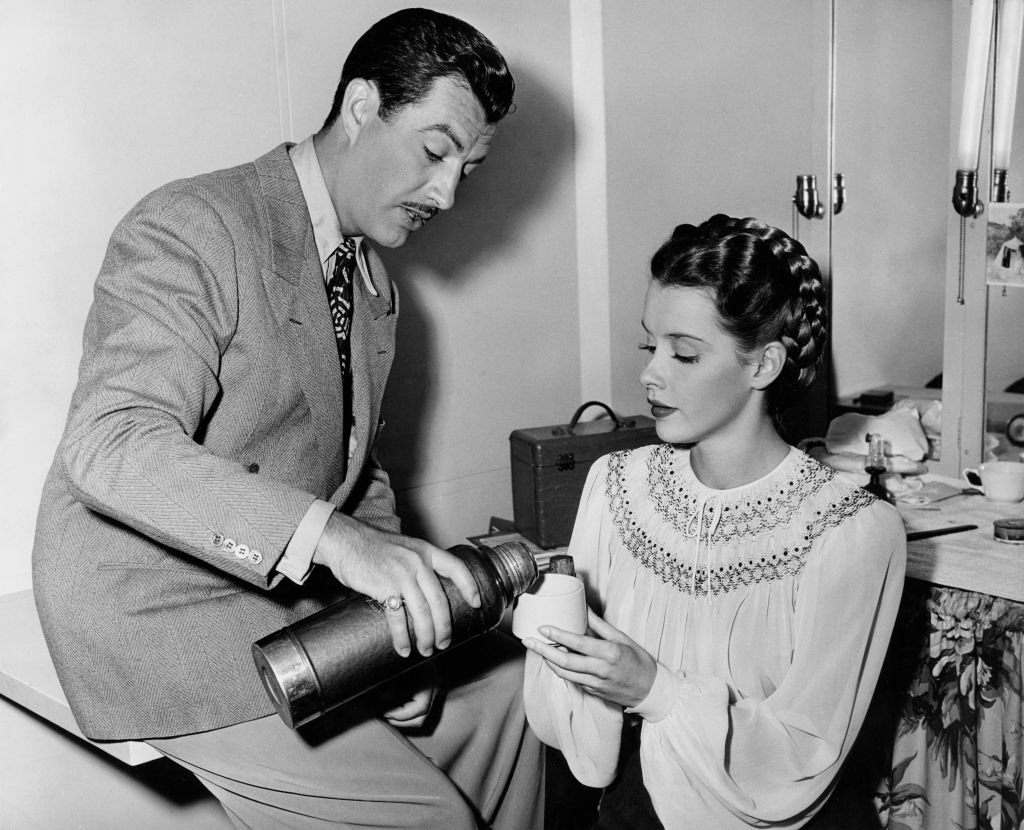 American actor Robert Taylor (1911 - 1969) pours coffee from a thermos flask for co-star Susan Peters (1921 - 1952) on the set of the film "Song of Russia" on July 9, 1943 | Source: Getty Images
