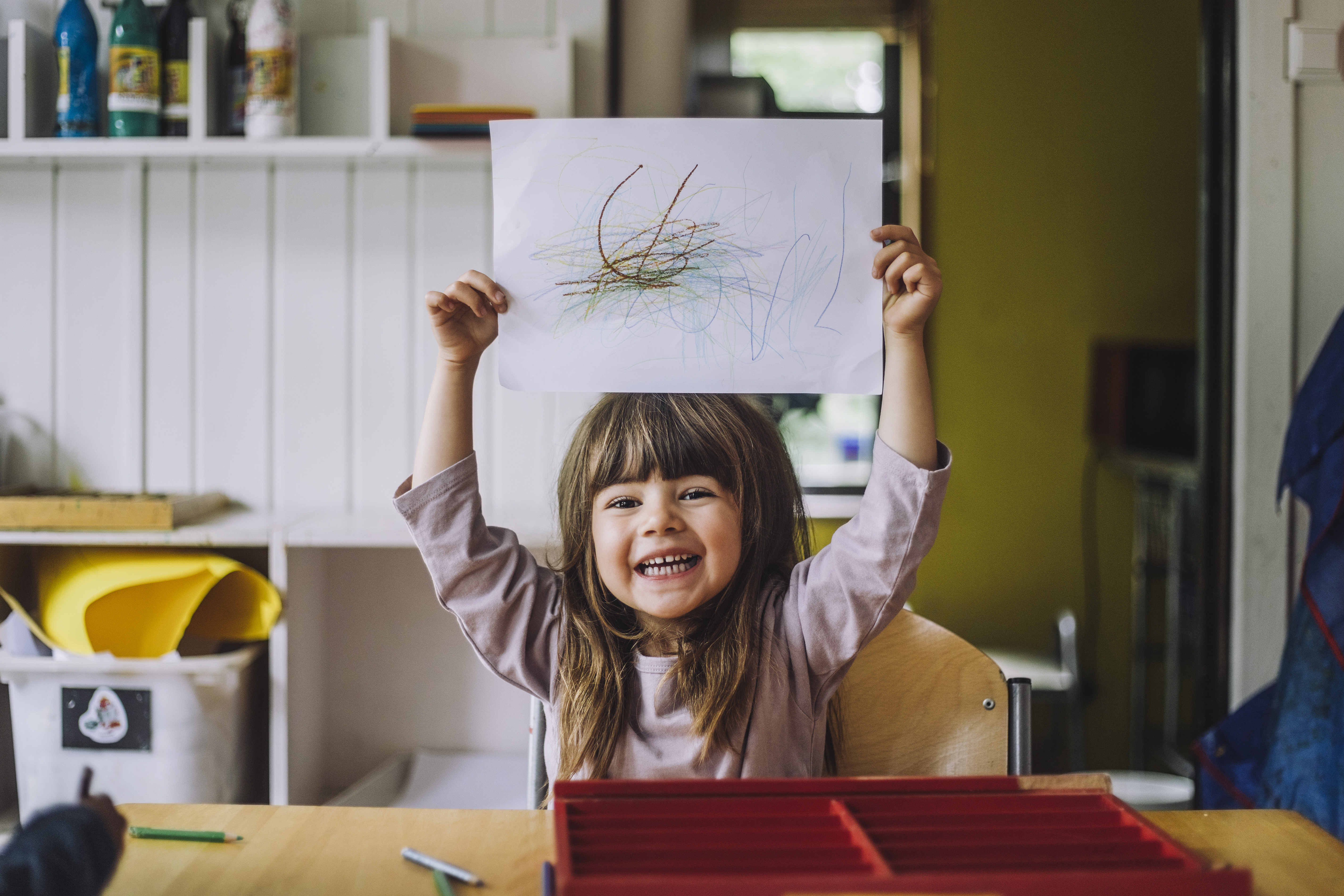 Happy little girl showing her colored pencil scribble on paper at kindergarten | Source: Getty Images