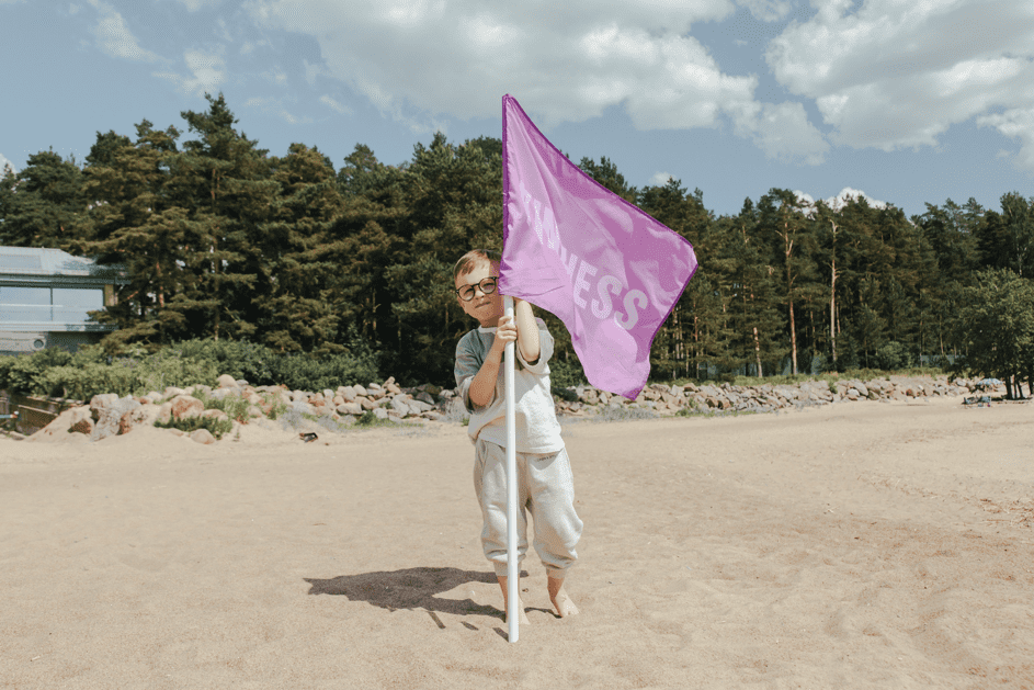 Ein Junge hält eine pinke Flagge mit dem Wort 'Güte' darauf. | Quelle: Pexels