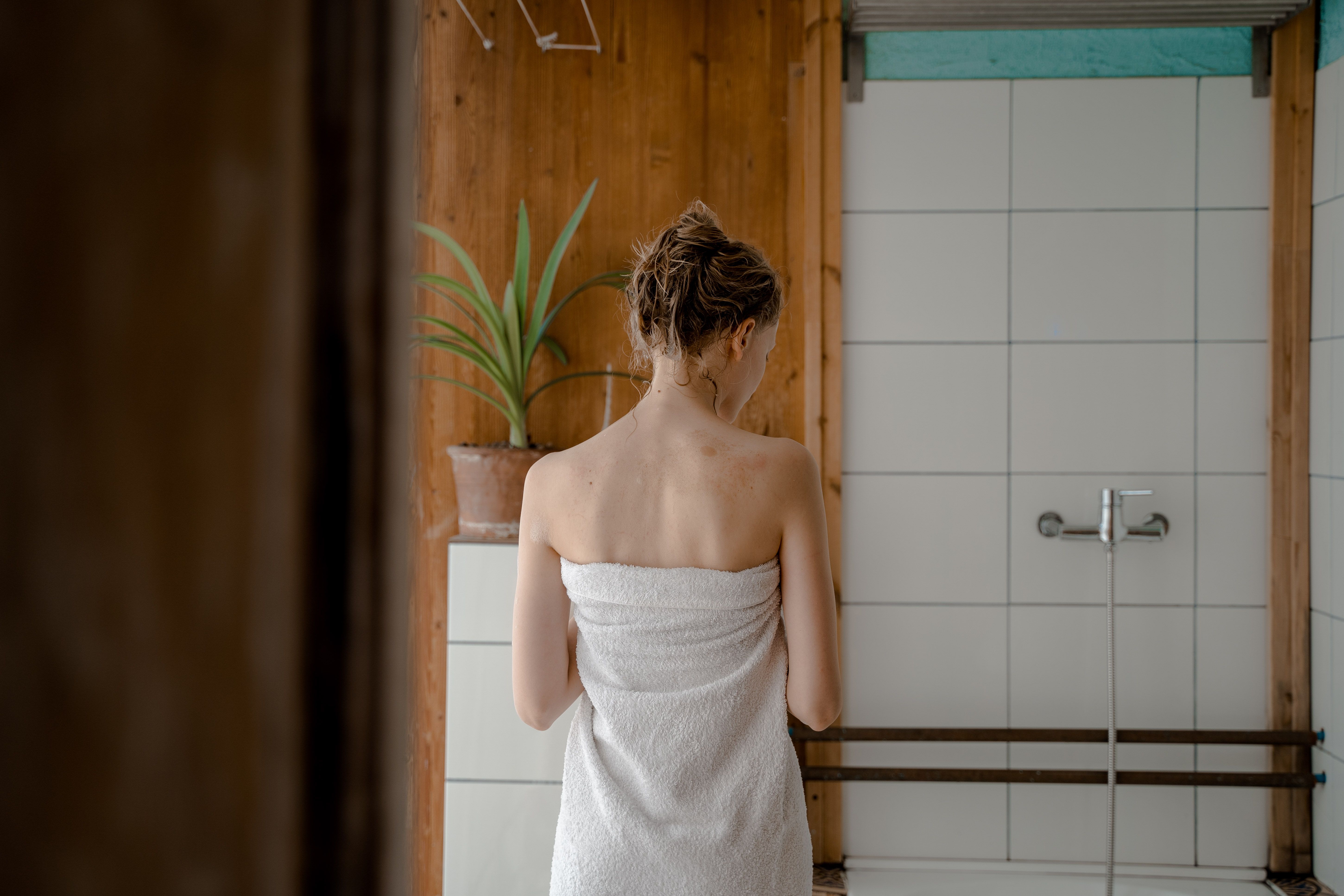 A woman wrapped in a towel stands inside a bathroom after bathing. | Source: Pexels