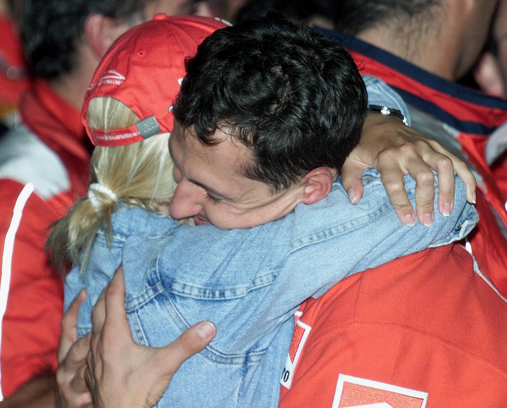 Ferrari driver Michael Schumacher (R) hugs Corinna Schumacher (L) in the pits to celebrate his victory in the Formula One Japanese Grand Prix as well as his 2000 Formula One World Championship title, after the race in Suzuka, on October 8, 2000. | Source: Getty Images
