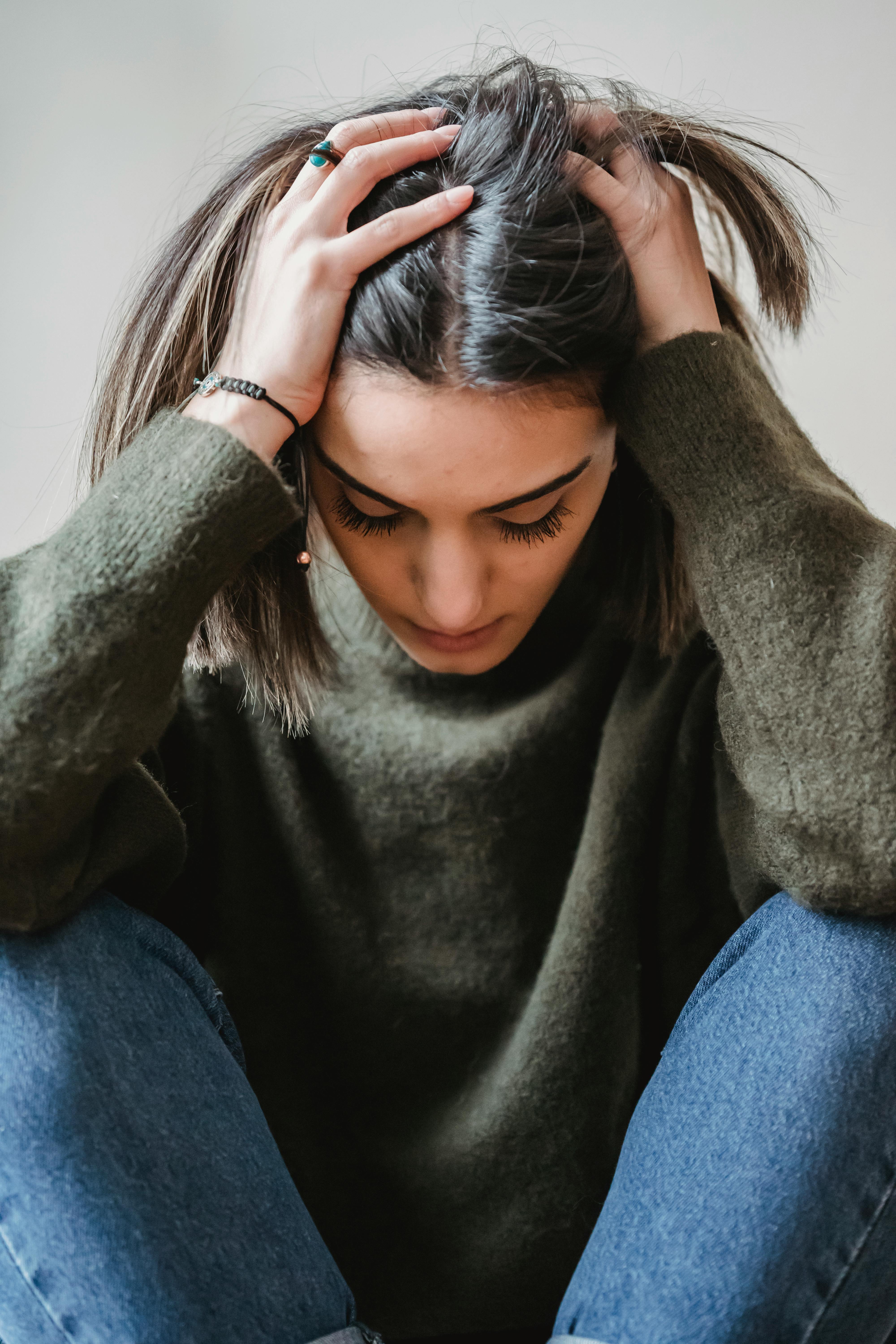 Woman running her hands through her hair and looking down in frustration | Source: Pexels