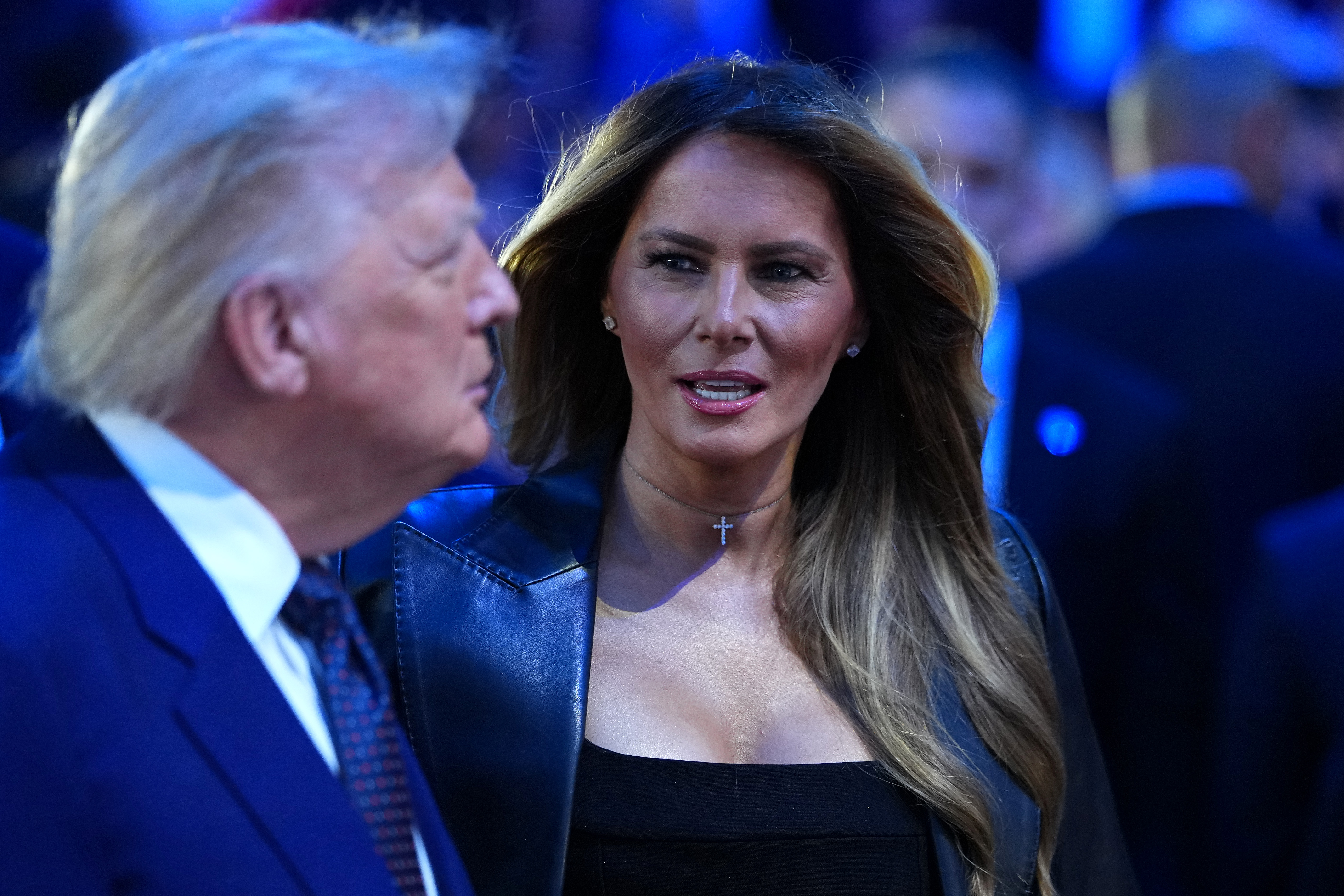 Melania Trump speaks with Donald Trump during the UFC event, her highlighted hair framing a smooth complexion and sharply defined facial contours under the venue lights.