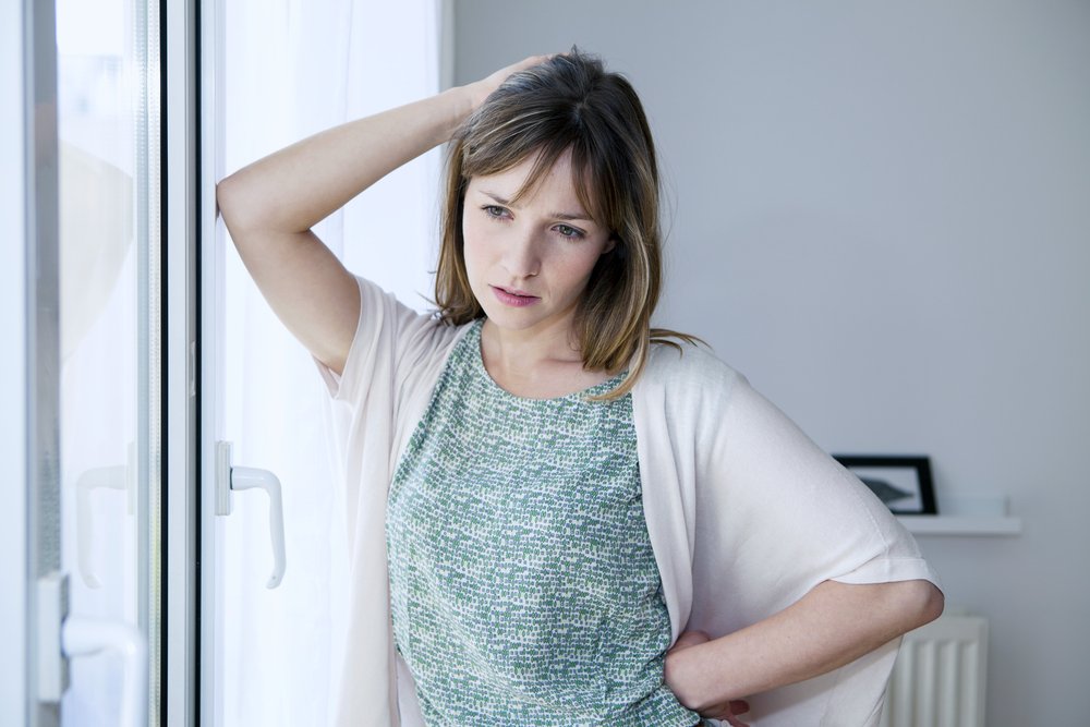 A photo of a worried woman standing by the windows. | Photo: Shutterstock