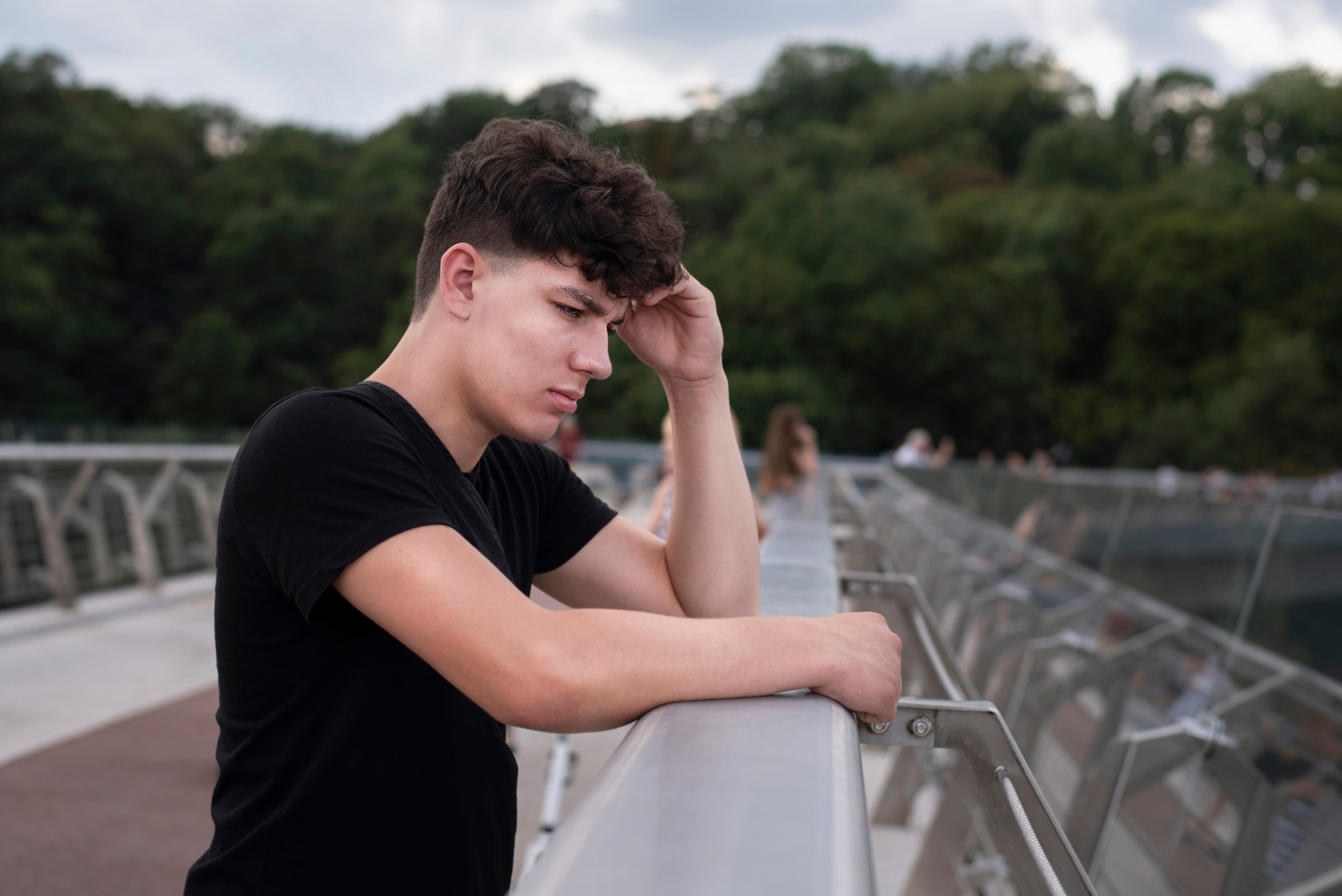 A sad teenage boy standing on a bridge overlooking a river | Source: Shutterstock