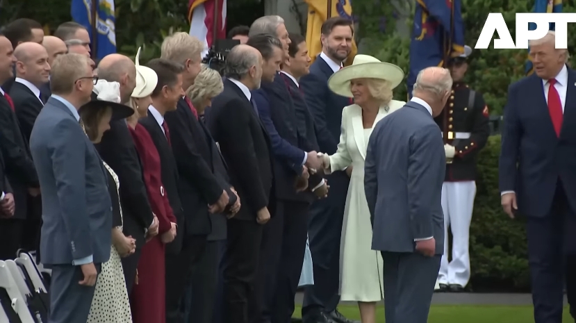 Queen Camilla steps forward with a smile to greet a member of the line, extending her hand as King Charles III turns slightly away, marking a continuation of the greeting order. | Source: YouTube/APT