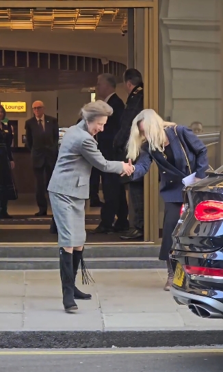Princess Anne shares a friendly handshake outside The Cumberland Hotel in London before departing, drawing attention to her polished appearance which included a fitted grey skirt suit, black tights, and her distinctive knee-high suede riding boots. | Source: Instagram/kingsguardchannel