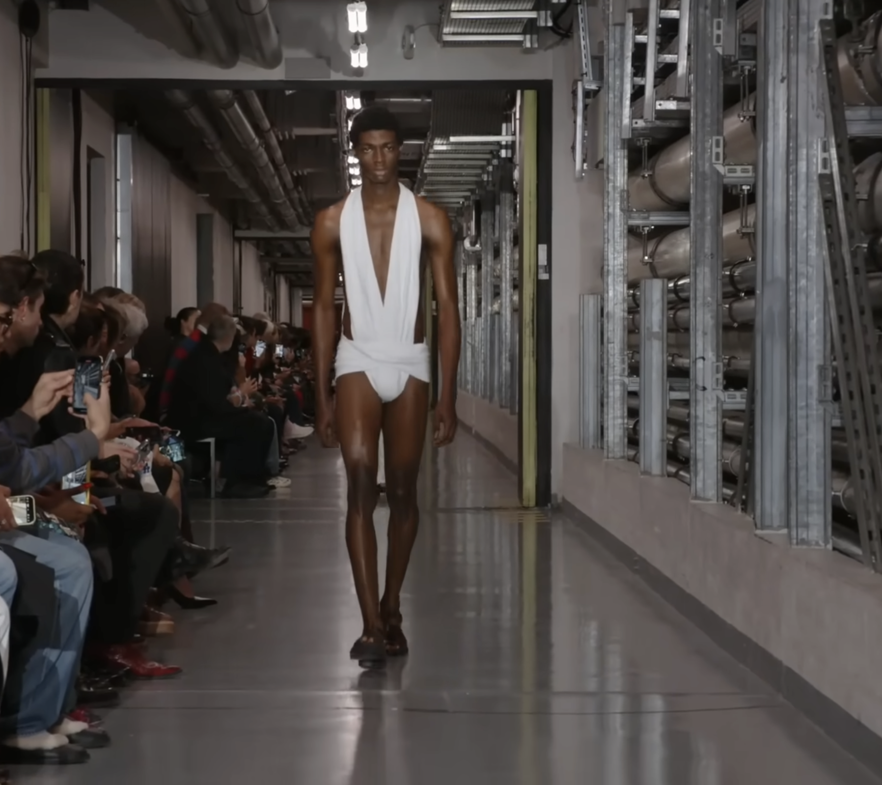 A male model followed, wearing another cutout bodysuit design. This time in white, glowing strikingly against his dark chocolate skin. The look hinted that futuristic fashion might draw from the past, with a loin section reminiscent of the Roman subligaculum. From a post dated October 5, 2025. Source: Youtube/@jeanpaulgaultier