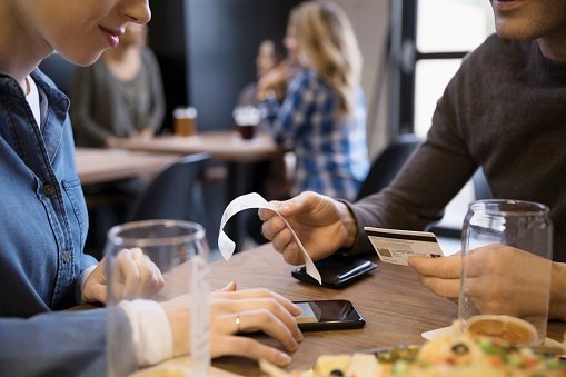 Close up couple with credit card paying bill calculating tip with smart phone in brewery restaurant | Photo: Getty Images