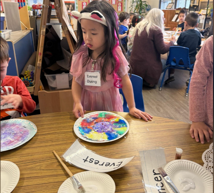 Everest Duong focuses on her colorful art project at a classroom table, her name tag pinned to her dress as she carefully works alongside classmates. | Source: GoFundMe