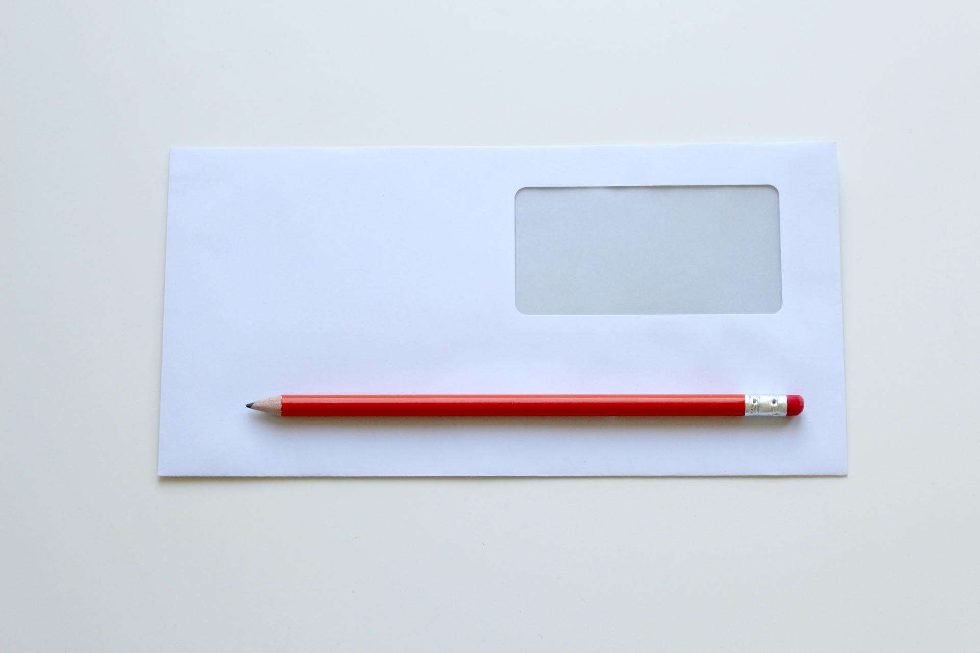 A red pencil on top of a white window envelope | Source: Pexels
