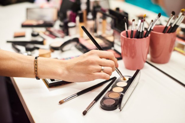 Mujer usando maquillaje en un tocador repleto de productos cosméticos.│Foto: Freepik