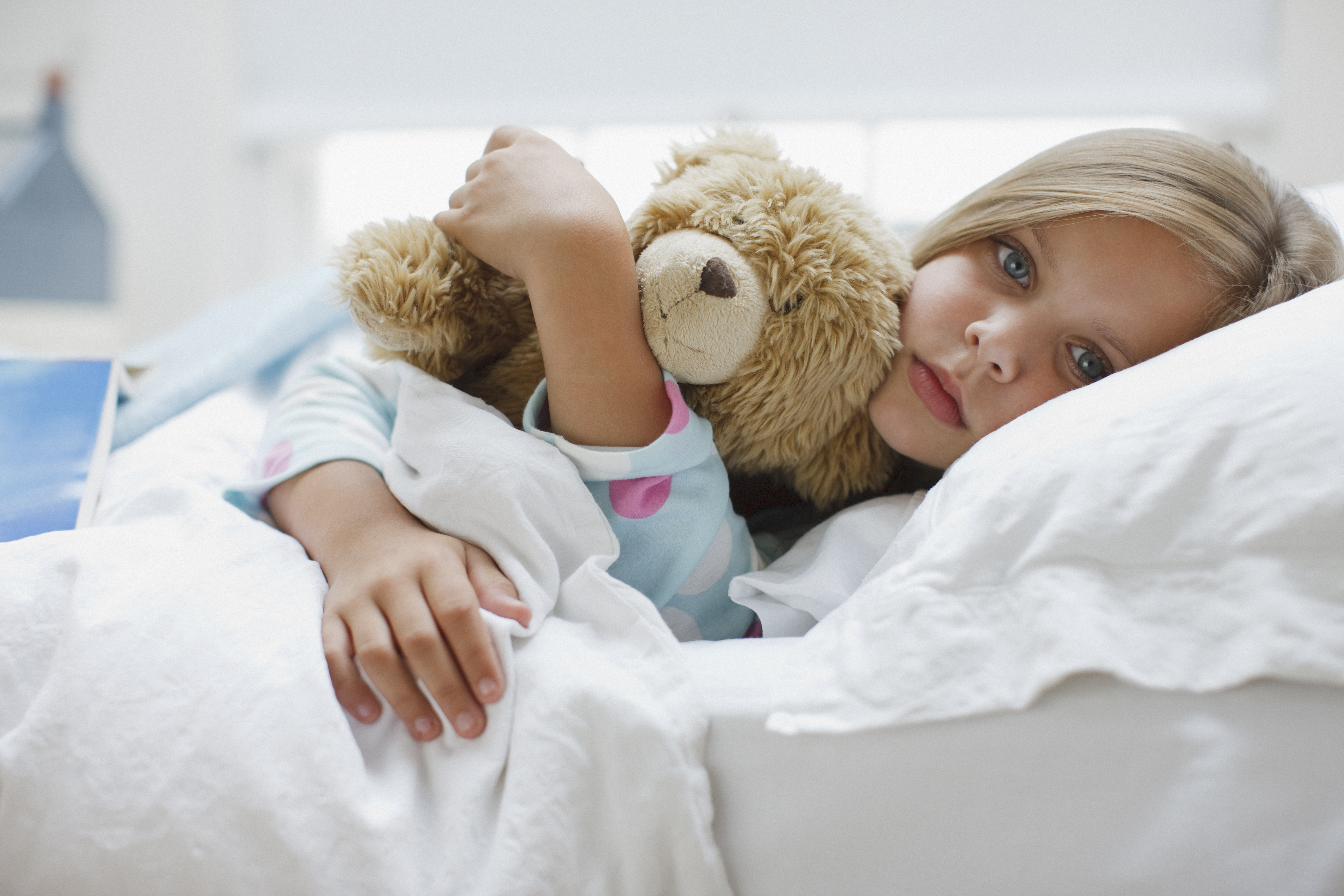 Sick girl laying in bed with teddy bear | Source: Getty Images
