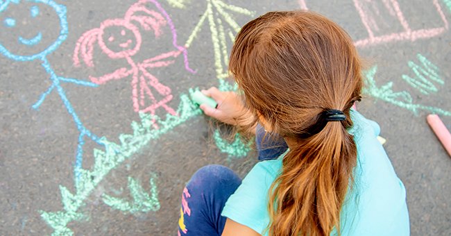 Little girl drawing pictures on the cement with chalk. | Source: Shutterstock 