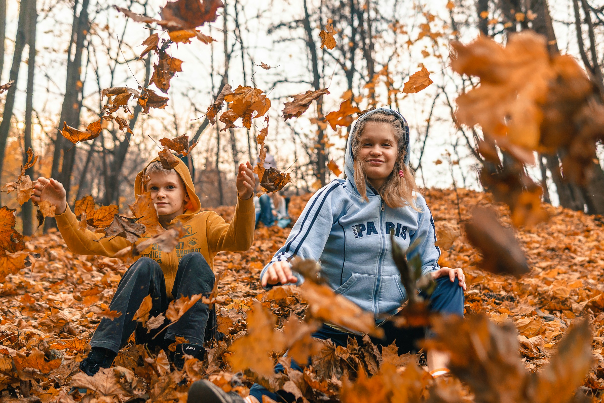 Two kids playing in fallen leaves | Source: Unsplash