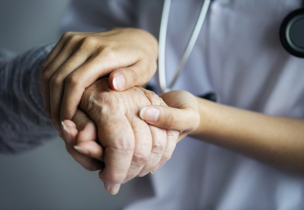 Empleado sanitario sosteniendo la mano de un anciano. │Foto: Freepik