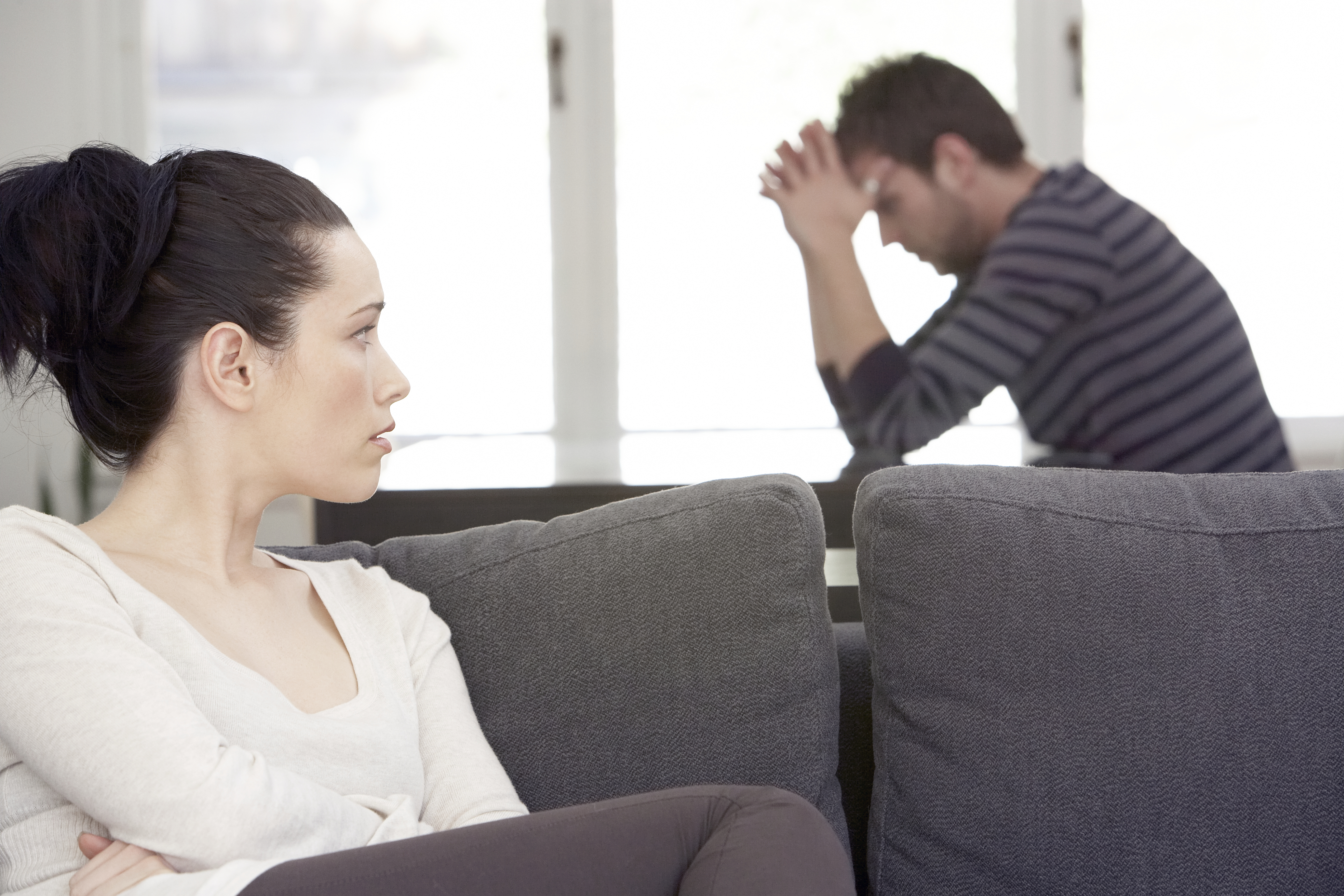 Young woman sitting on sofa, looking at distressed man at table | Source: Getty Images