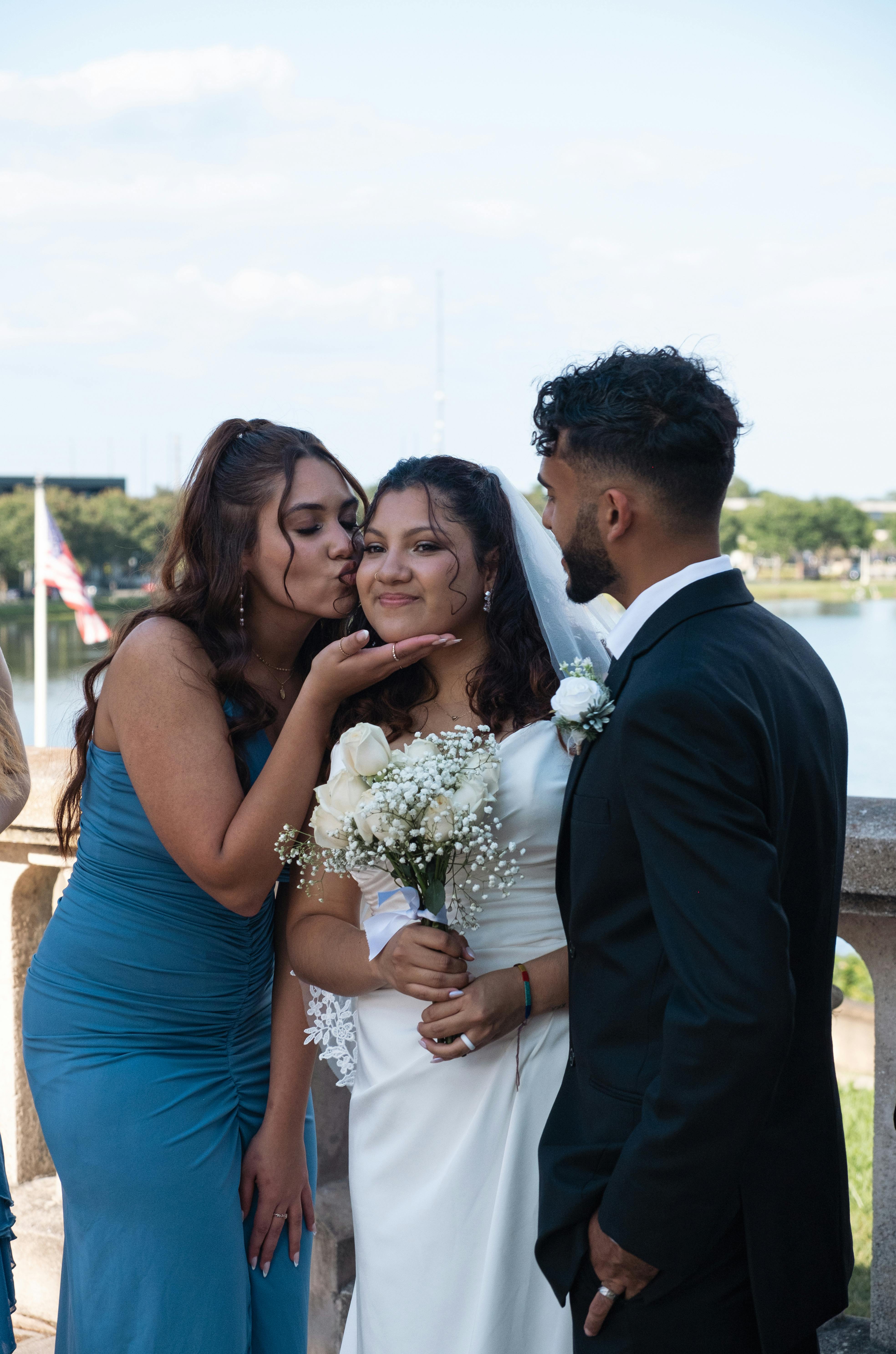 A bridesmaid kissing the bride while the groom looks on | Source: Pexels