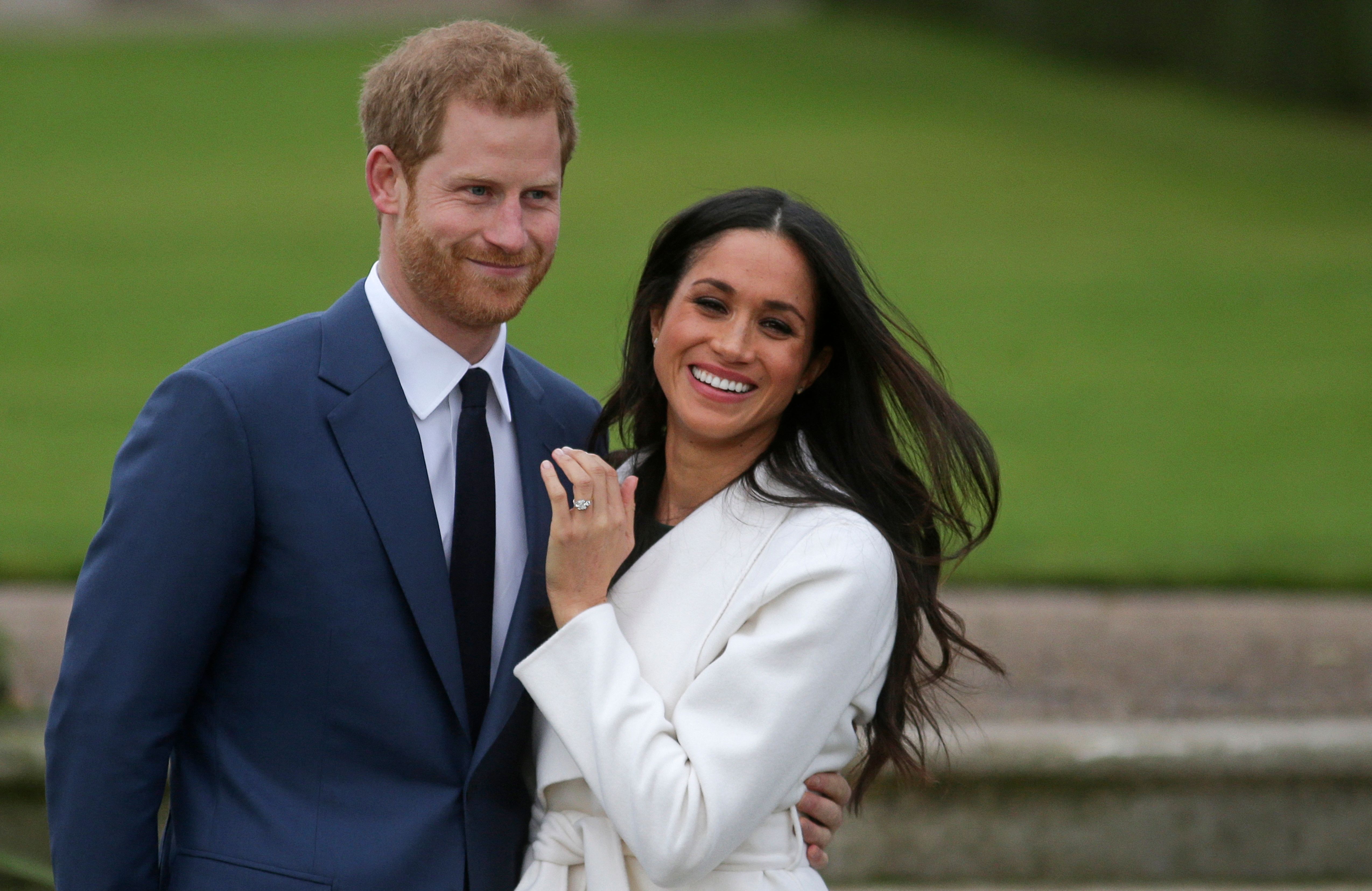 Britain's Prince Harry stands with his fiancée US actress Meghan Markle as she shows off her engagement ring while they pose for a photograph in the Sunken Garden at Kensington Palace in west London on November 27, 2017, following the announcement of their engagement. | Source: Getty Images