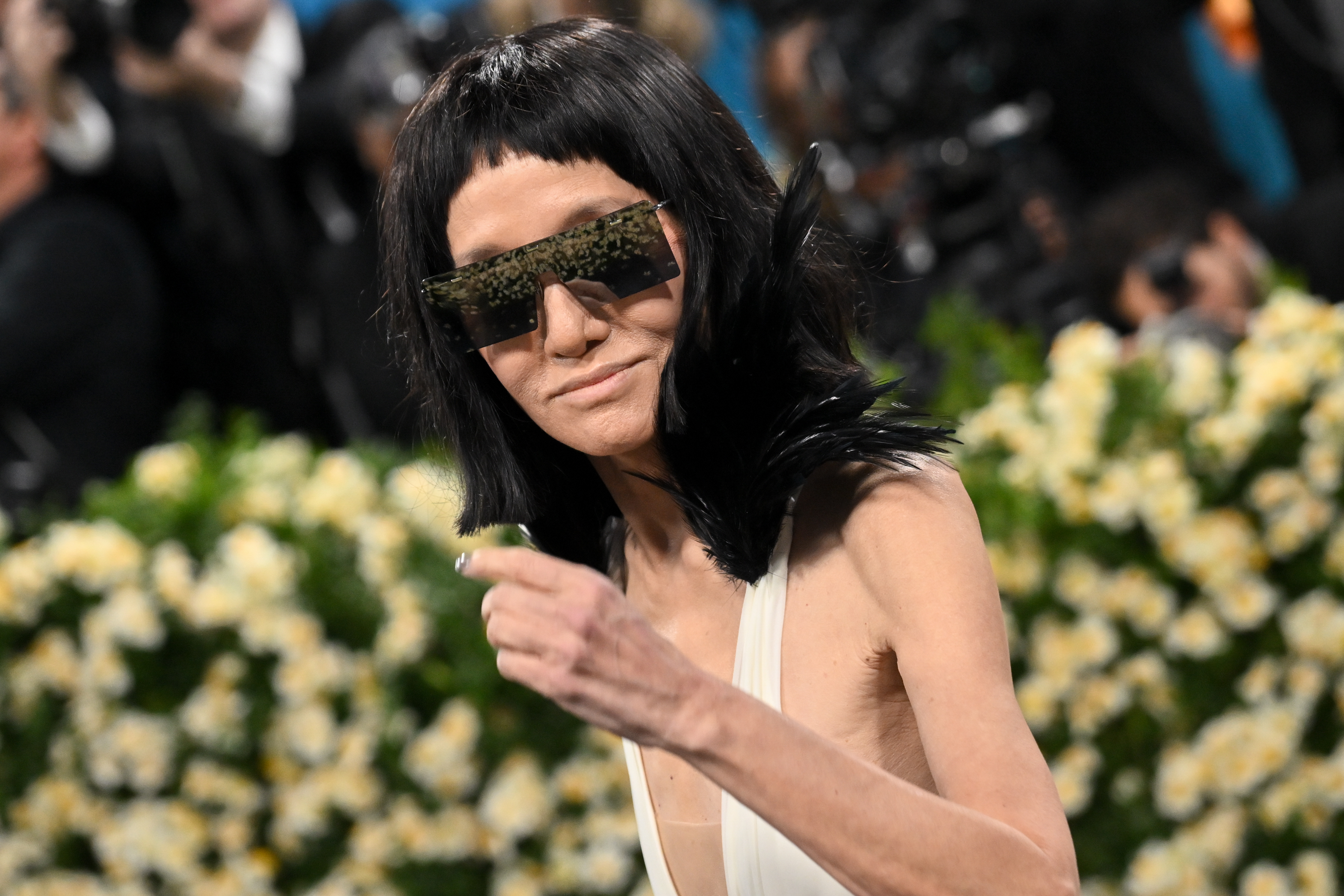 In a candid moment, Vera Wang gestures to the crowd while her mirrored sunglasses and feathered neckline reflect the energy of the evening.
