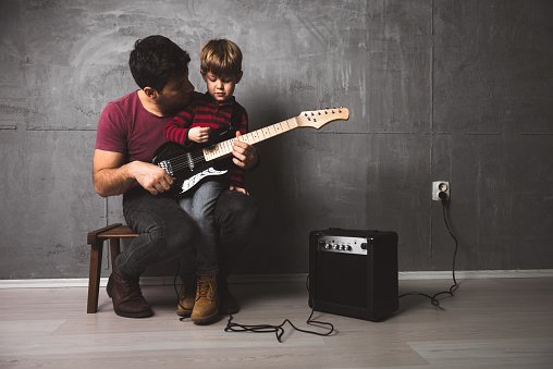 Photo of father and son playing guitar and singing in the microphone in the basement. | Photo: Getty Images