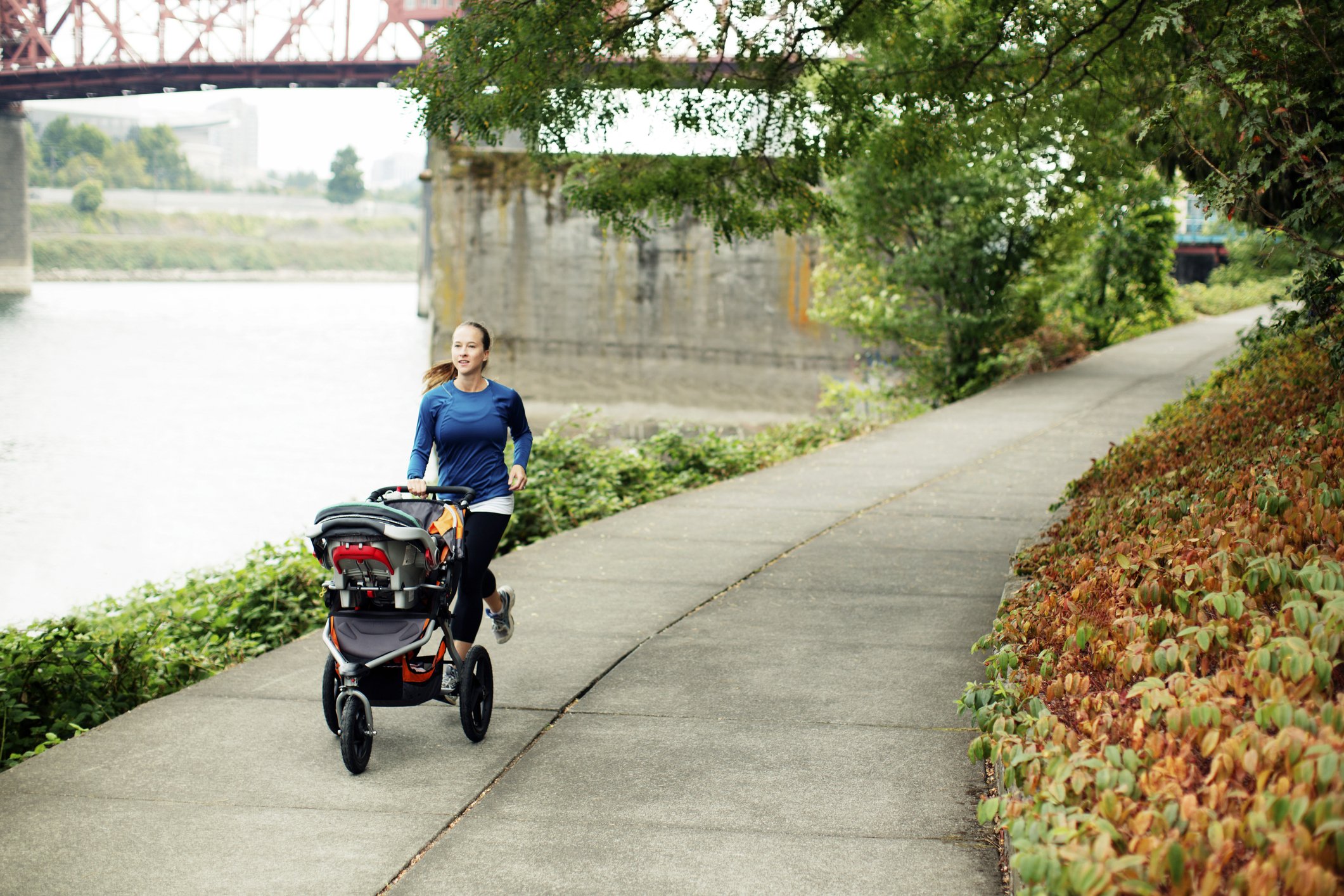 Frau joggt mit Kinderwagen auf einem Fußweg am Fluss | Quelle: Getty Images