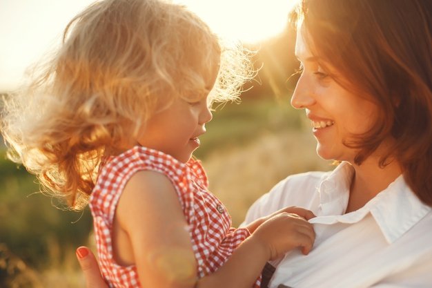 Mujer sosteniendo sosteniendo risueña a una niña. │Foto: Freepik