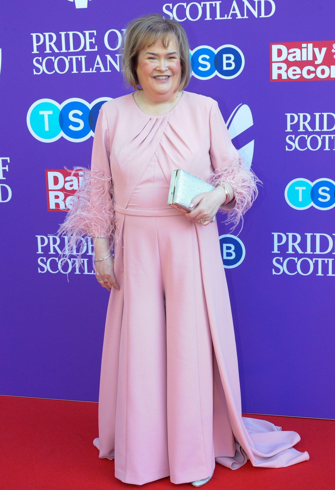 Boyle cuts a glamorous figure on the red carpet at the "Pride of Scotland Awards 2024" in Glasgow on 20 May, wearing a blush-pink wide-leg jumpsuit with feathered cuffs and carrying a glittering clutch bag.