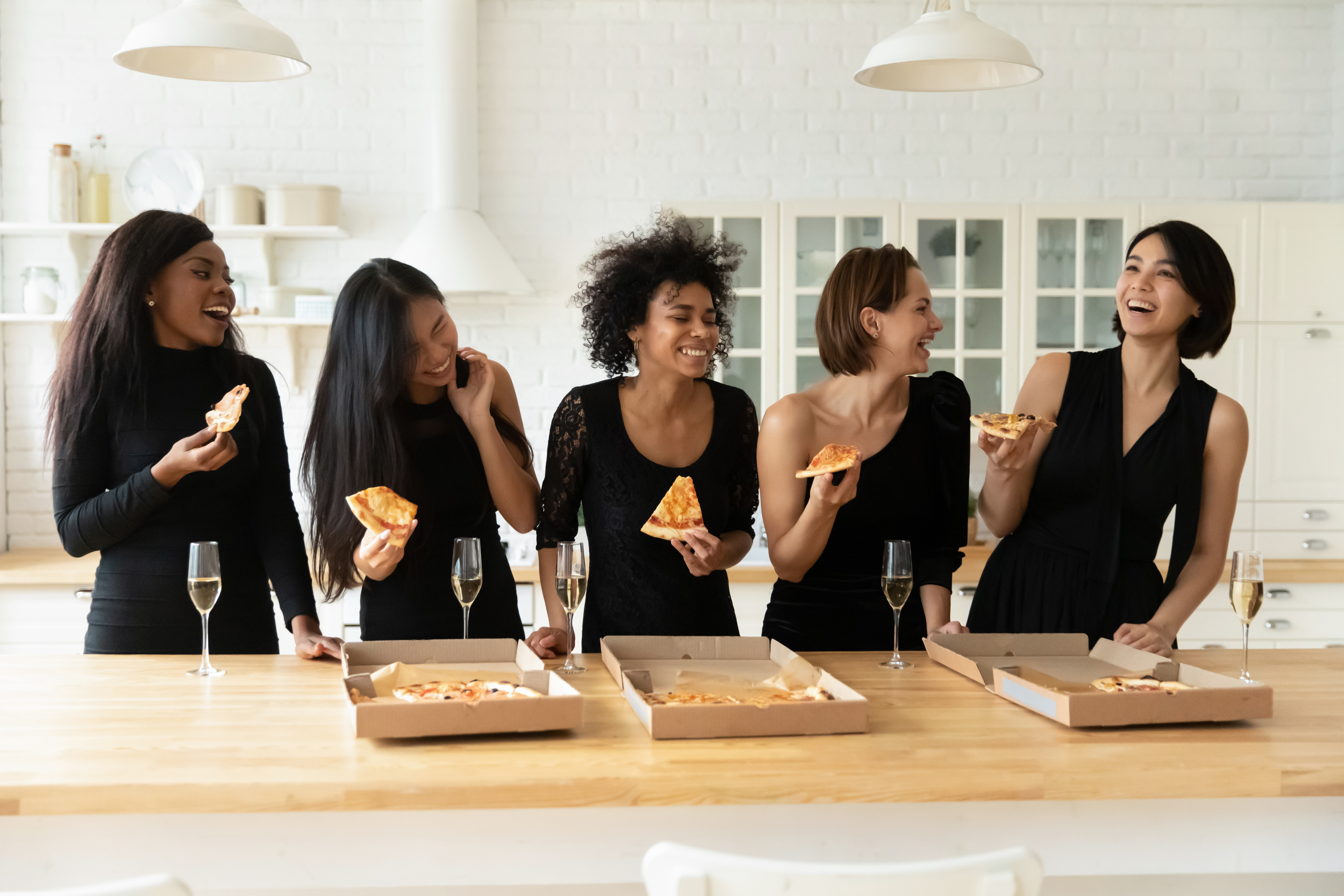 Women wearing black eating pizza and drinking champagne | Source: Shutterstock