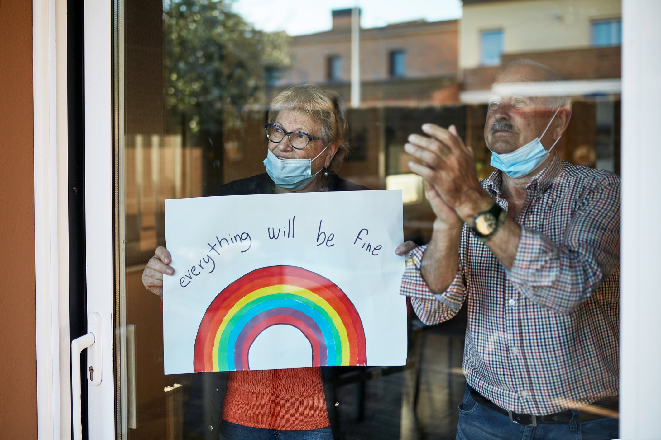 Älteres Paar in den 70ern klatscht in die Hände, als es einen handgezeichneten Regenbogen zu Hause in Quarantäne zeigt | Quelle: Getty Images