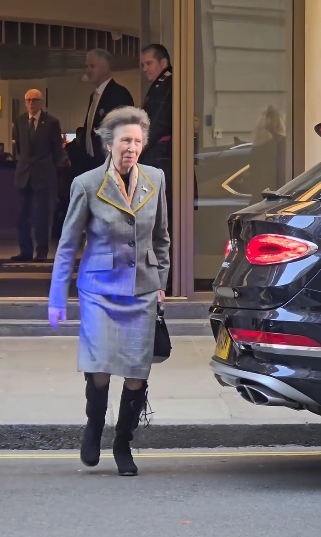 Princess Anne walks along the pavement outside The Cumberland Hotel in London, carrying a small black handbag while her structured grey skirt suit and polished knee-high suede riding boots stand out as she makes her way toward a waiting vehicle nearby. | Source: Instagram/kingsguardchannel