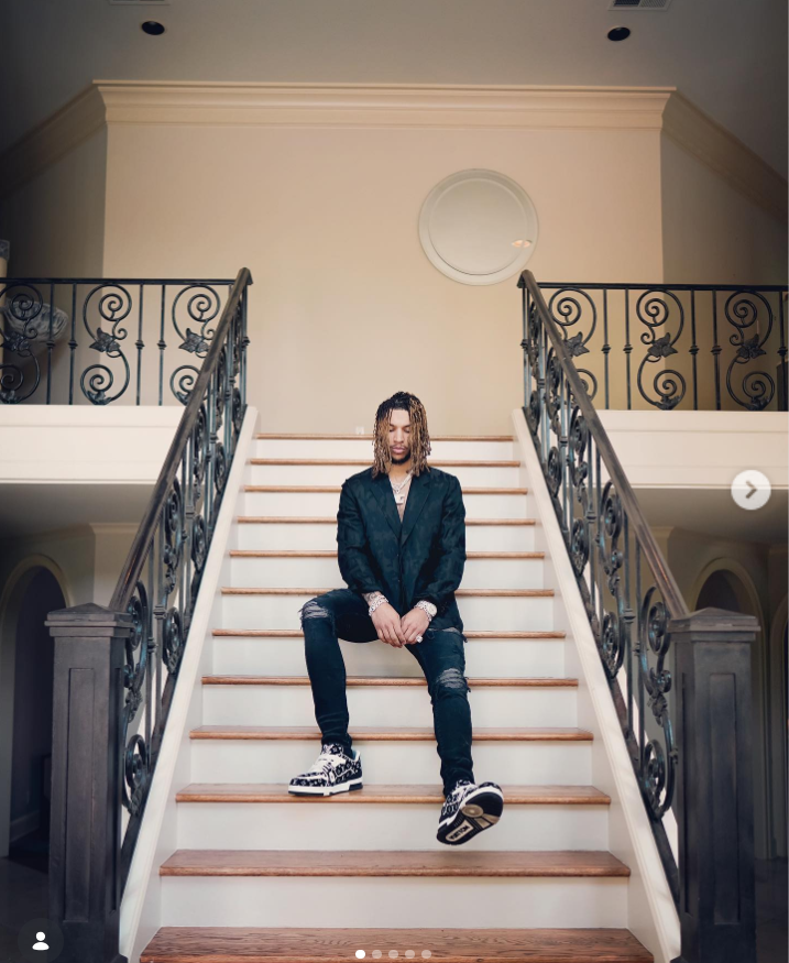 Brandon Clarke sits on a staircase inside a large home while wearing a black jacket, ripped jeans, and patterned sneakers. | Source: Instagram/brandon_clarke23
