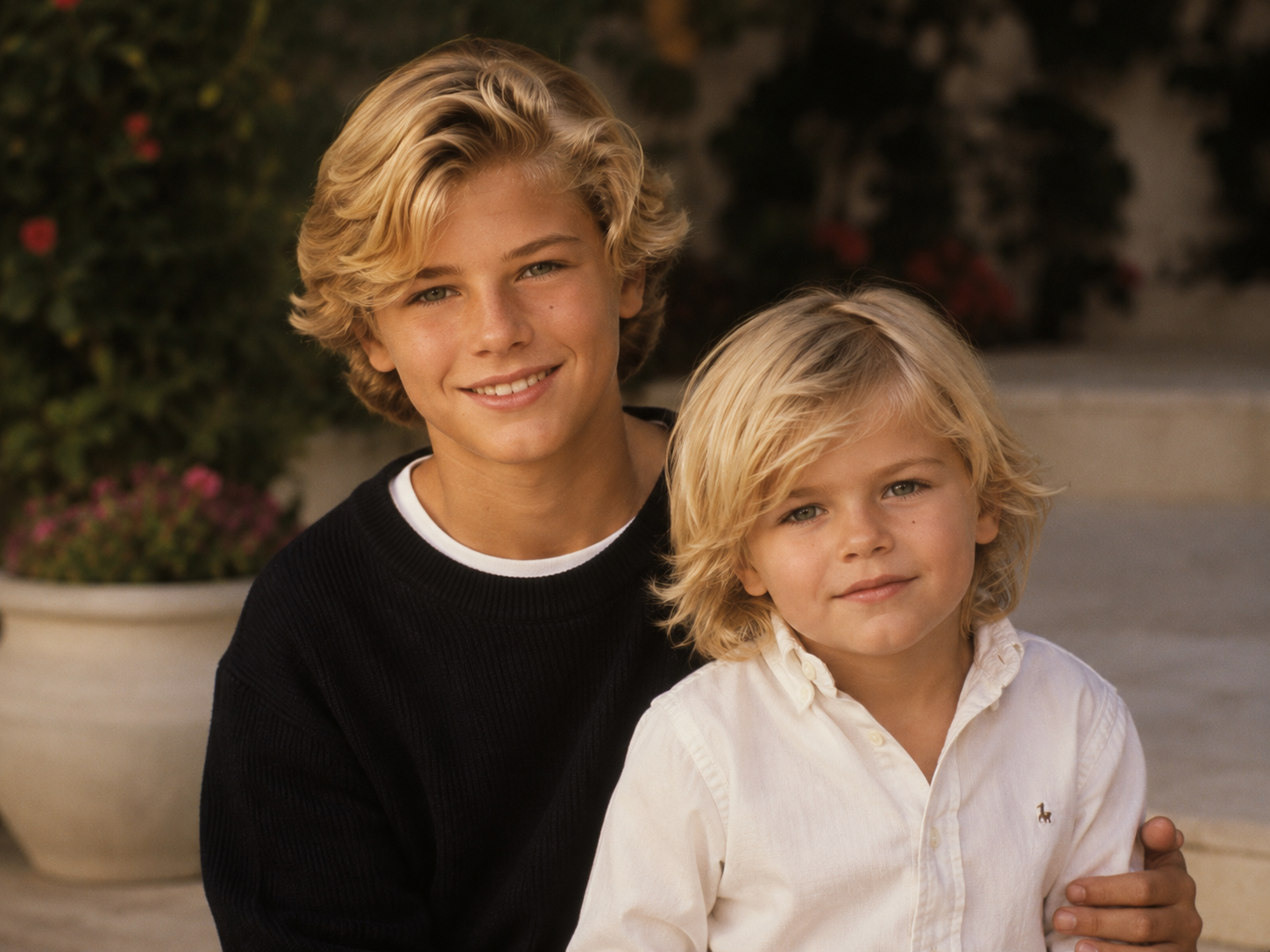 In an AI-generated image, Fabio and Anna Nicole Smith’s imagined sons pose together outdoors in a warm, relaxed portrait featuring matching feathered blonde hair and preppy attire. | Source: ChatGPT
