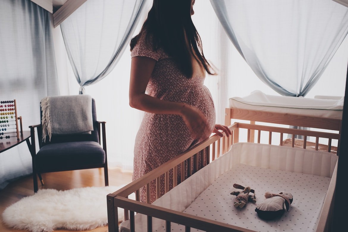 Mujer embarazada mira con ternura la cuna del bebé. | Foto: Unsplash