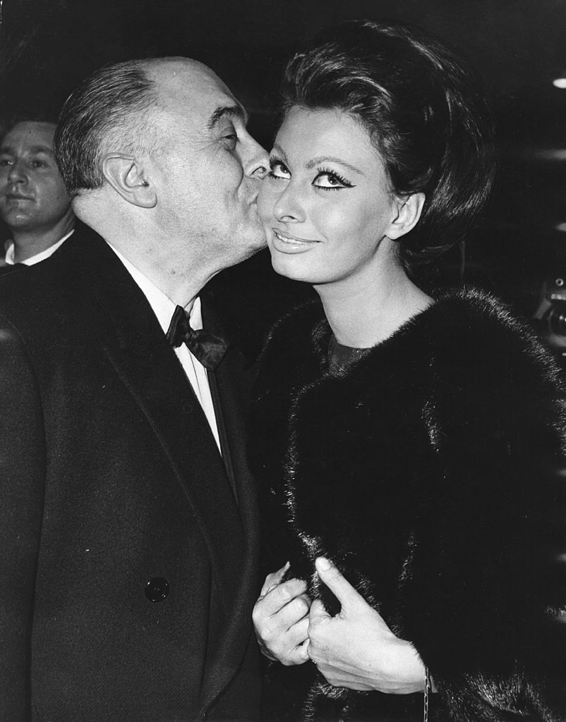 Le producteur de cinéma italien Carlo Ponti embrasse sa femme, l'actrice Sophia Loren, après qu'elle a reçu le premier prix Alexander Korda, la nommant "Star internationale de l'année", lors de la première mondiale de son nouveau film "Lady L" à l'Empire, le 26 novembre 1965 | Photo : Getty Images