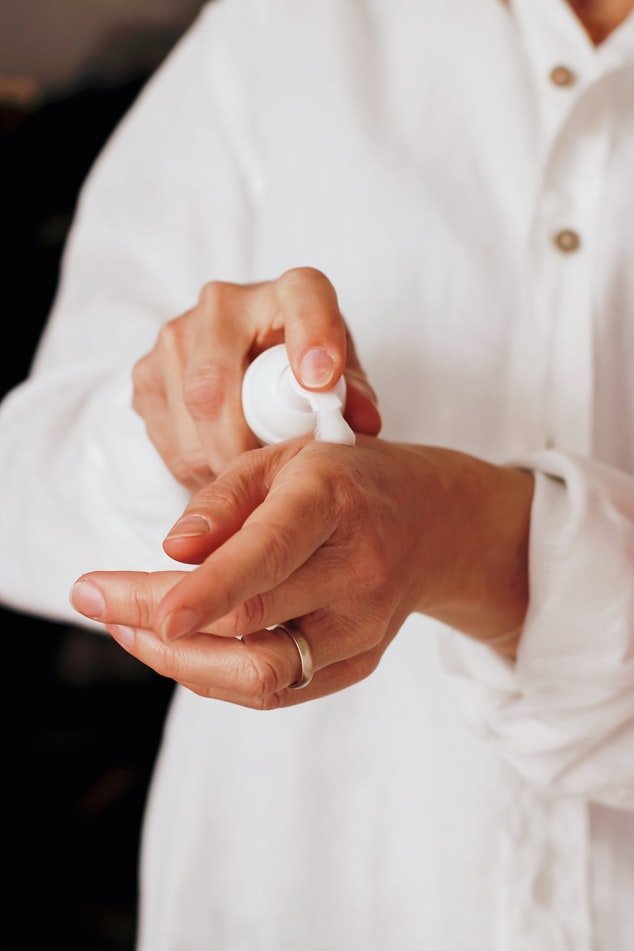 Une femme appliquant de la crème sur la peau de ses mains. l Source : Unsplash