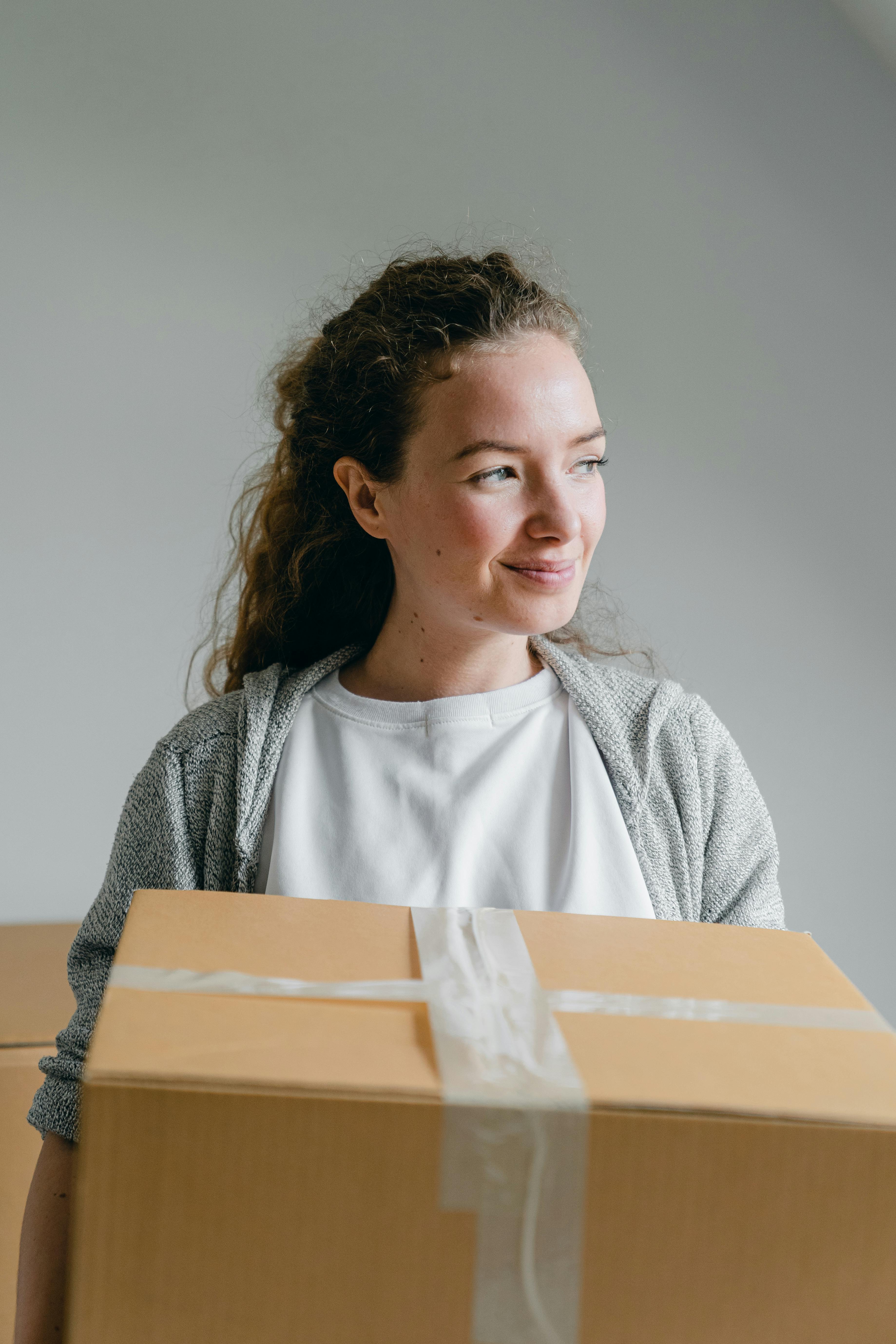 A smiling woman holding a taped box | Source: Pexels