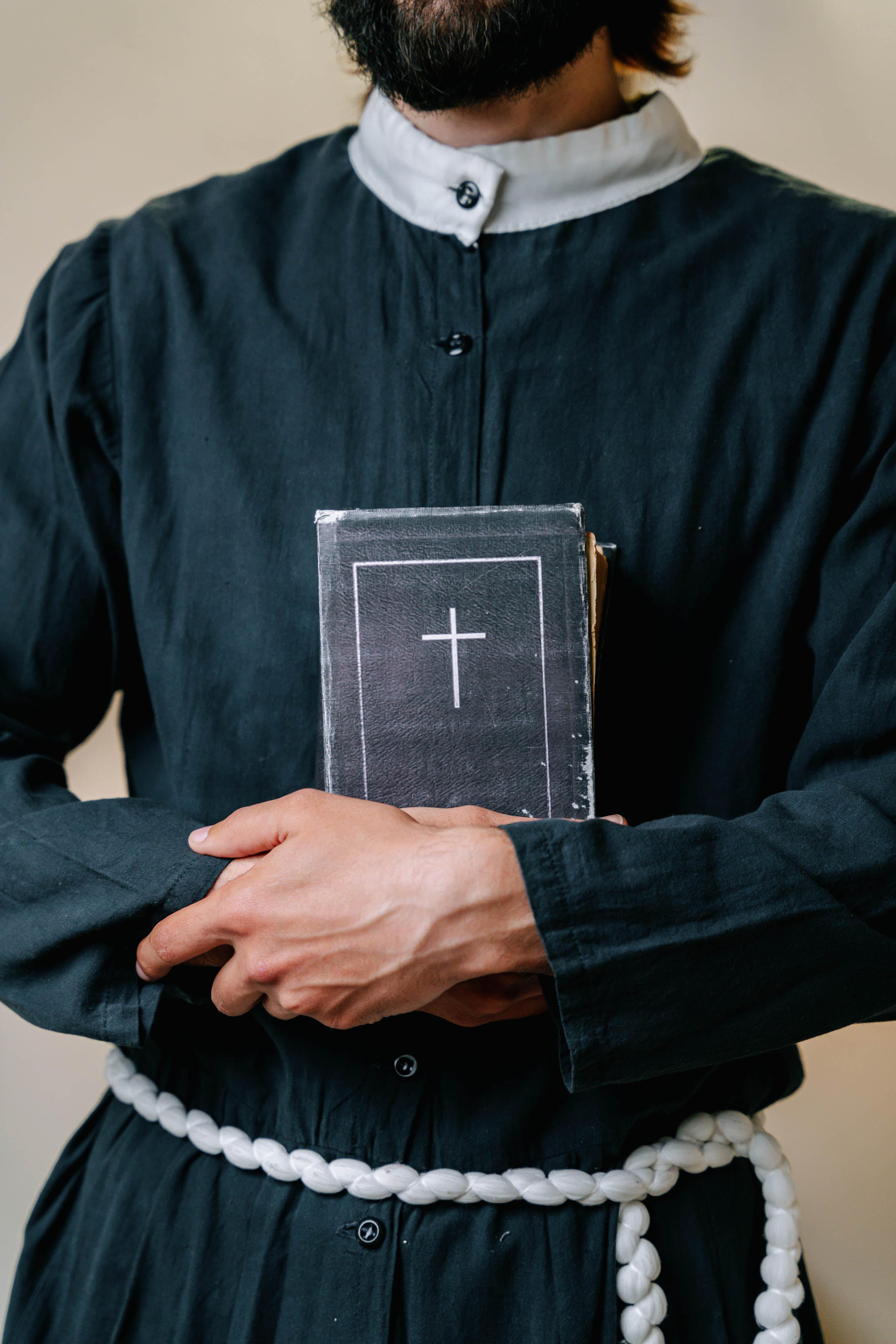 A man wearing a cassock holding a Holy Bible. | Source: Pexels