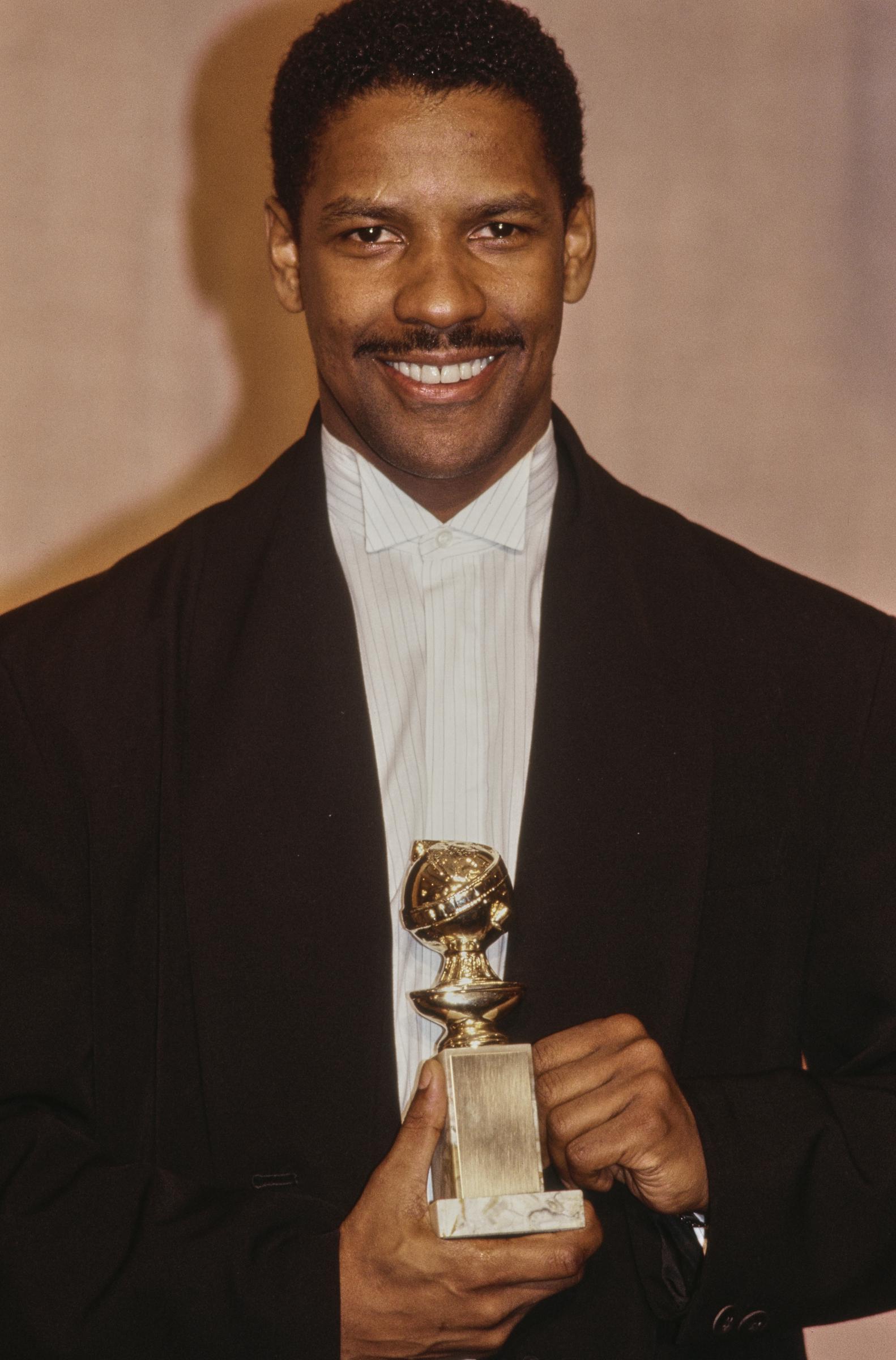 Denzel Washington beams in the press room after winning a Golden Globe for "Glory." His trimmed, black hair and mustache mirror the composed, classic style that defined his performance.