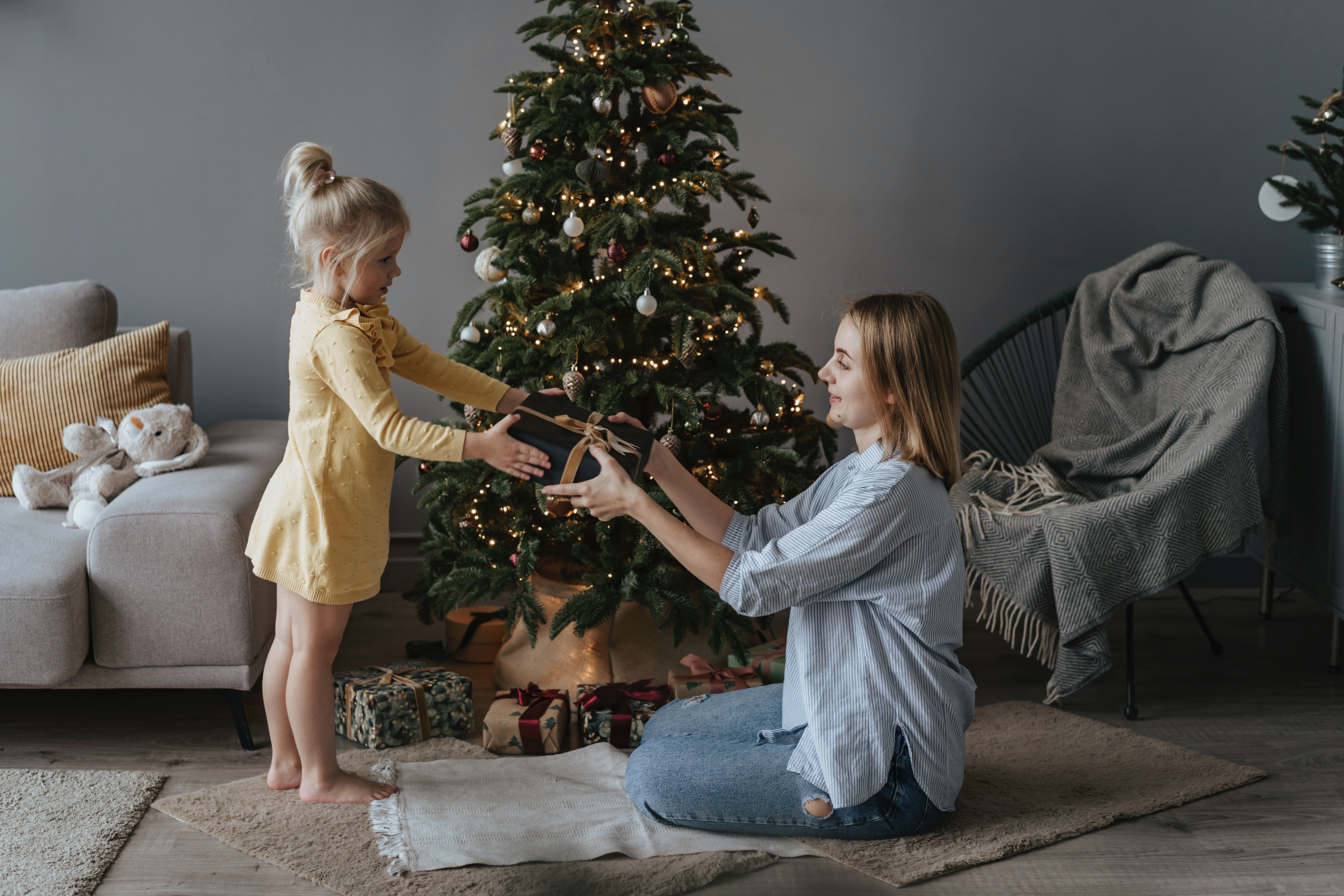 Una niña da un regalo a su madre frente al árbol de navidad. | Foto: Pexels