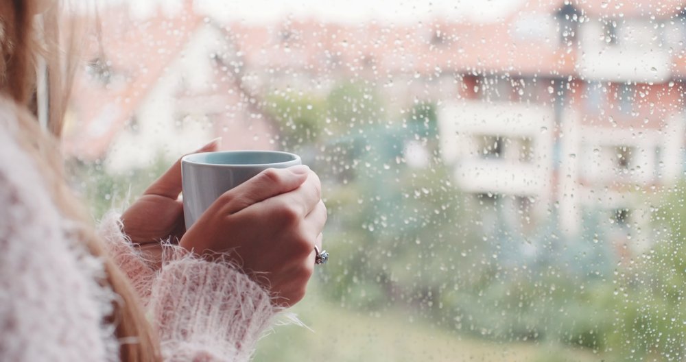 A photo of a woman with a cup of coffee looking out the window. | Photo: Shutterstock