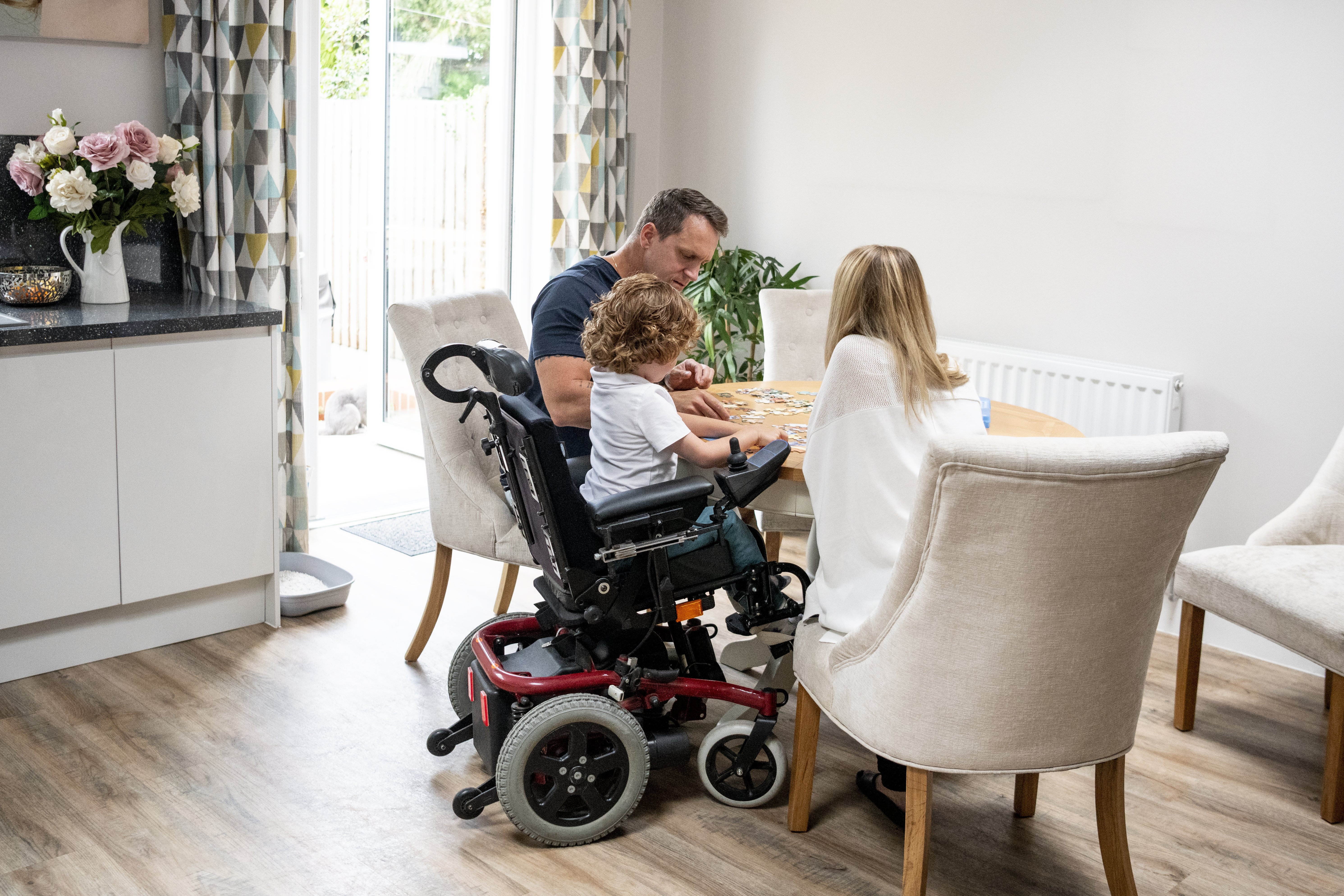 6 year old boy with muscular dystrophy, sitting at dining table with mother and father, playing a game, quality time with family|Photo: Getty Images