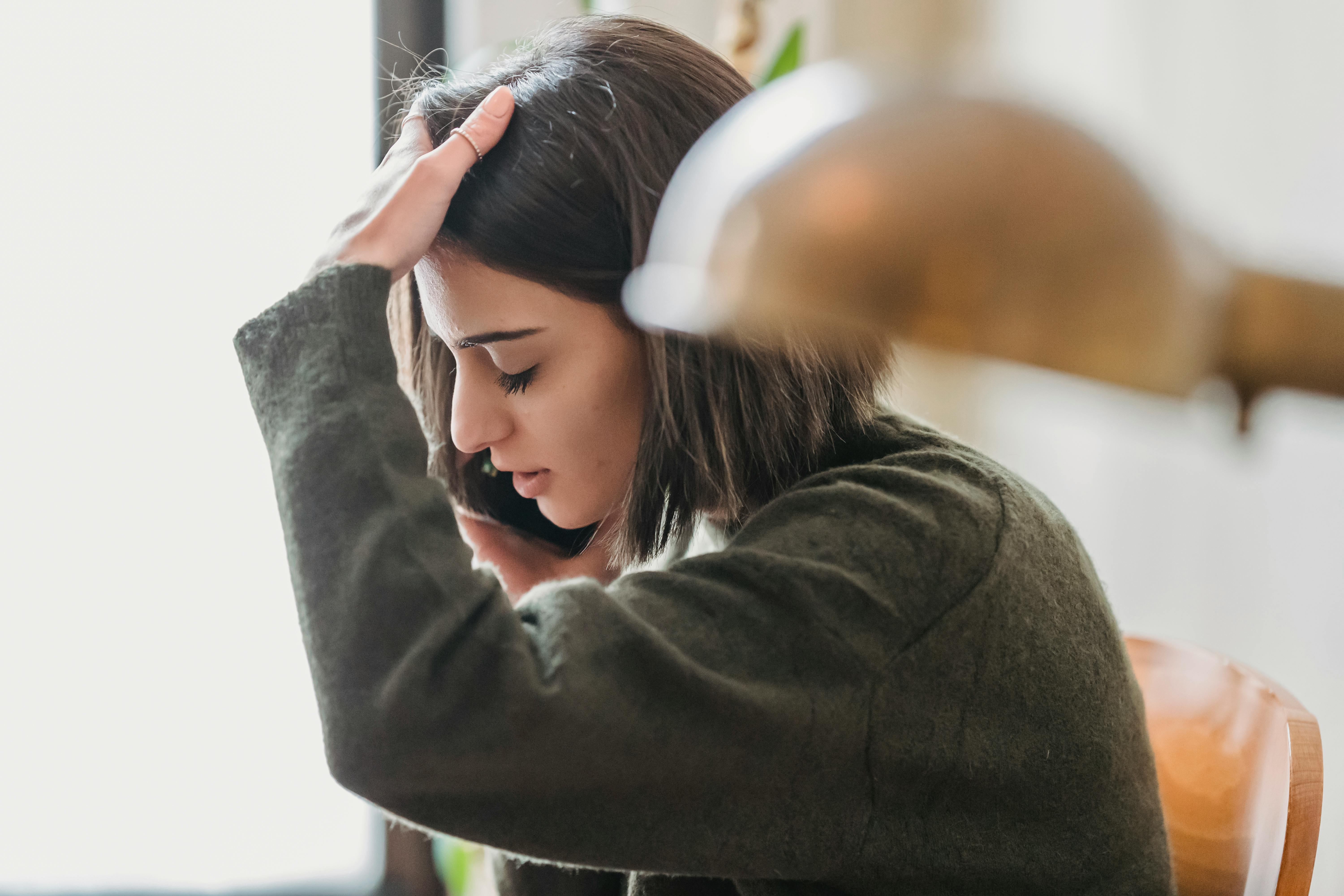 A young woman touching her head while talking on the phone | Source: Pexels